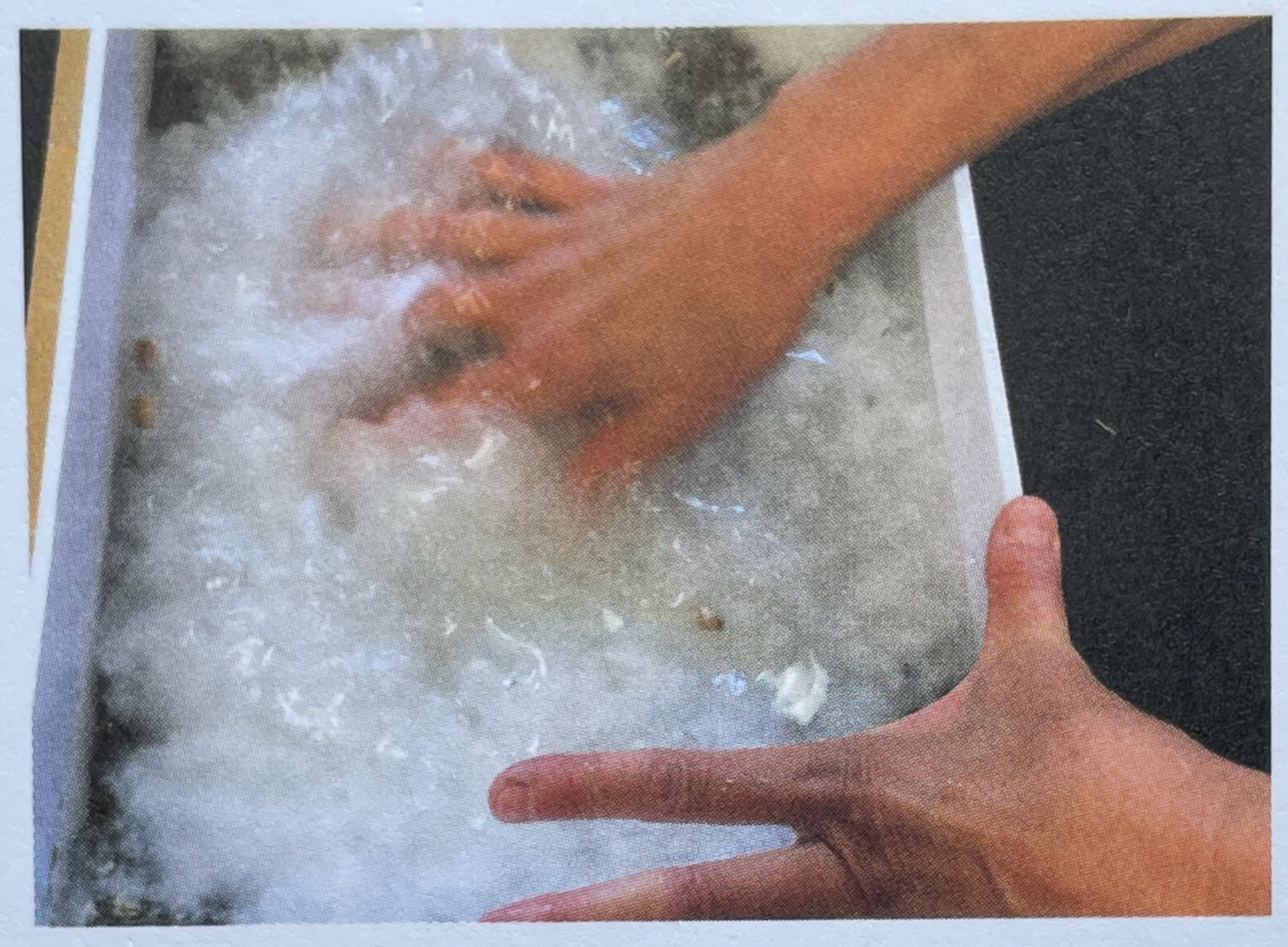 Two hands submerged in a box of white, fluffy substance, possibly foam or soft material, with one hand actively manipulating it.