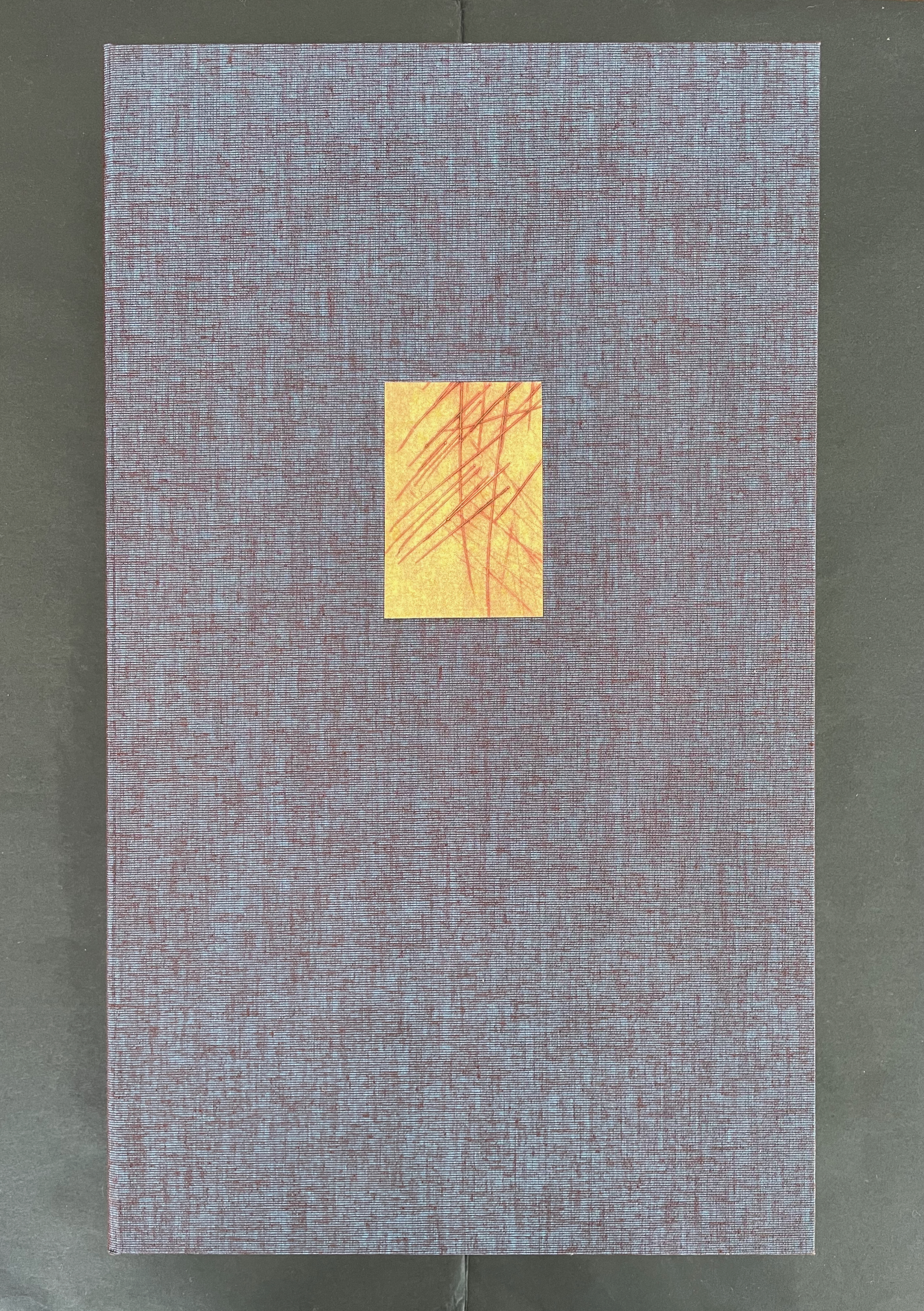 A textured book cover with a dark purple fabric background and a small square cutout featuring a yellow-orange paper with red lines.