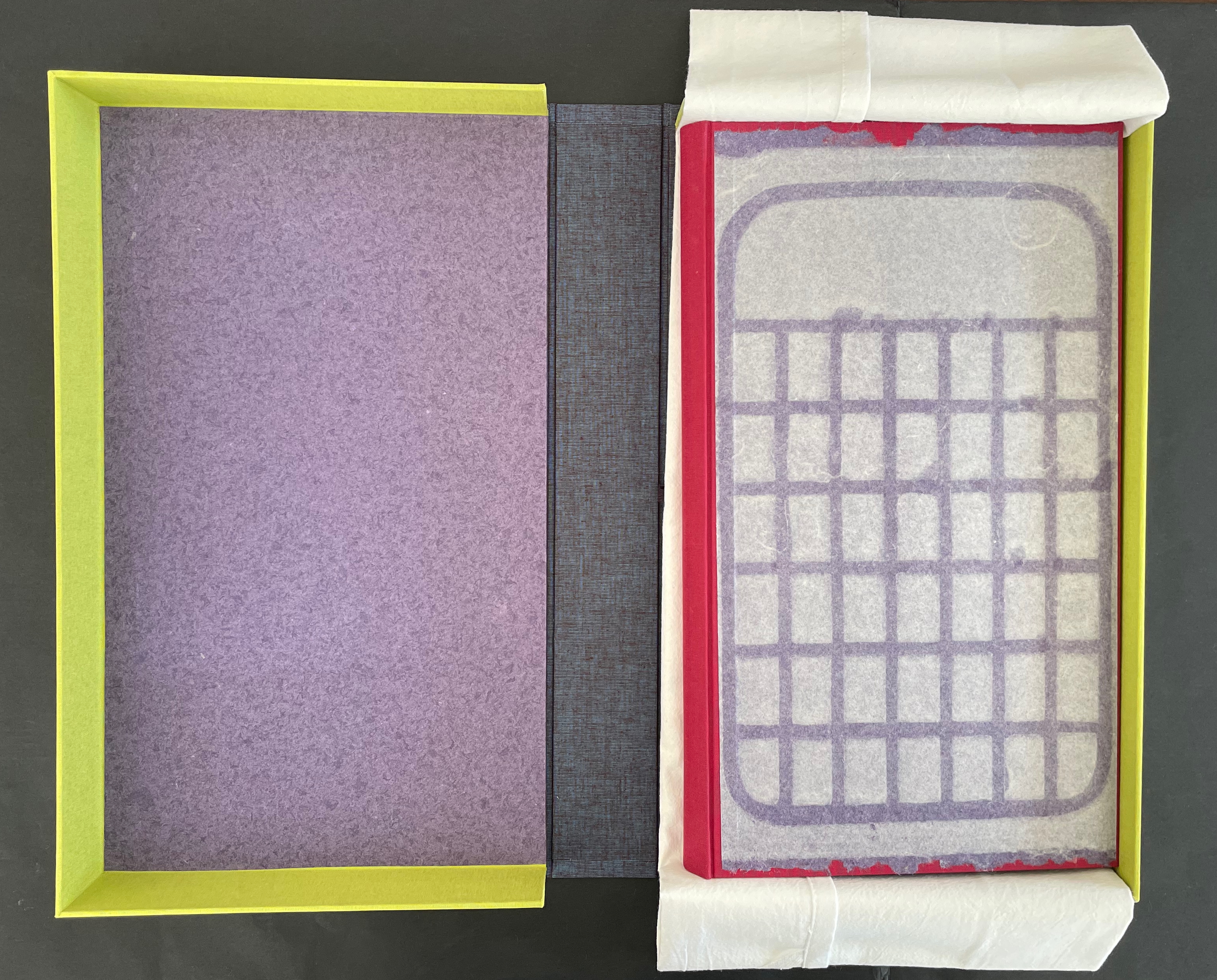 An open box with a yellow border showcasing a purple interior, a grayish-blue outer layer, and a sheet of parchment paper laid over a red base featuring a grid pattern.