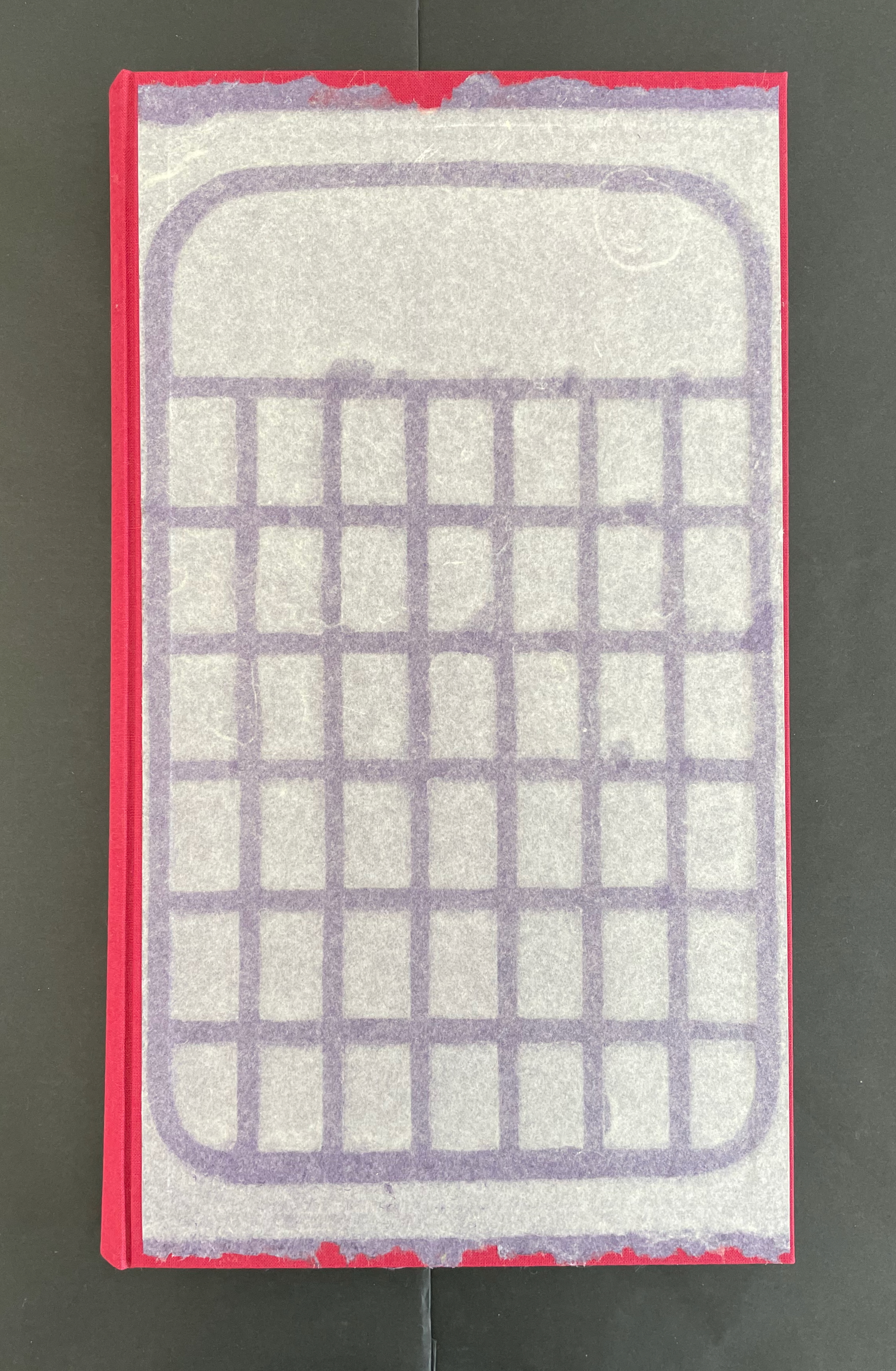 Top view of a book with a red spine and a paper cover featuring a grid pattern in purple.