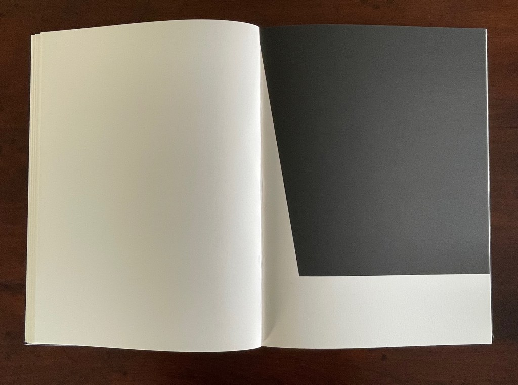An open book with a blank white page on the left and a dark gray page on the right, creating a striking contrast.