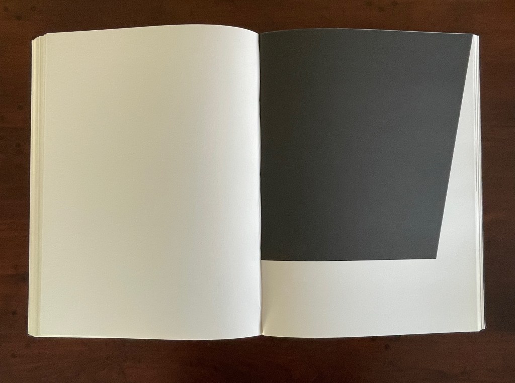 An open book displaying two pages, one with a blank white page and the other featuring a black geometric shape.