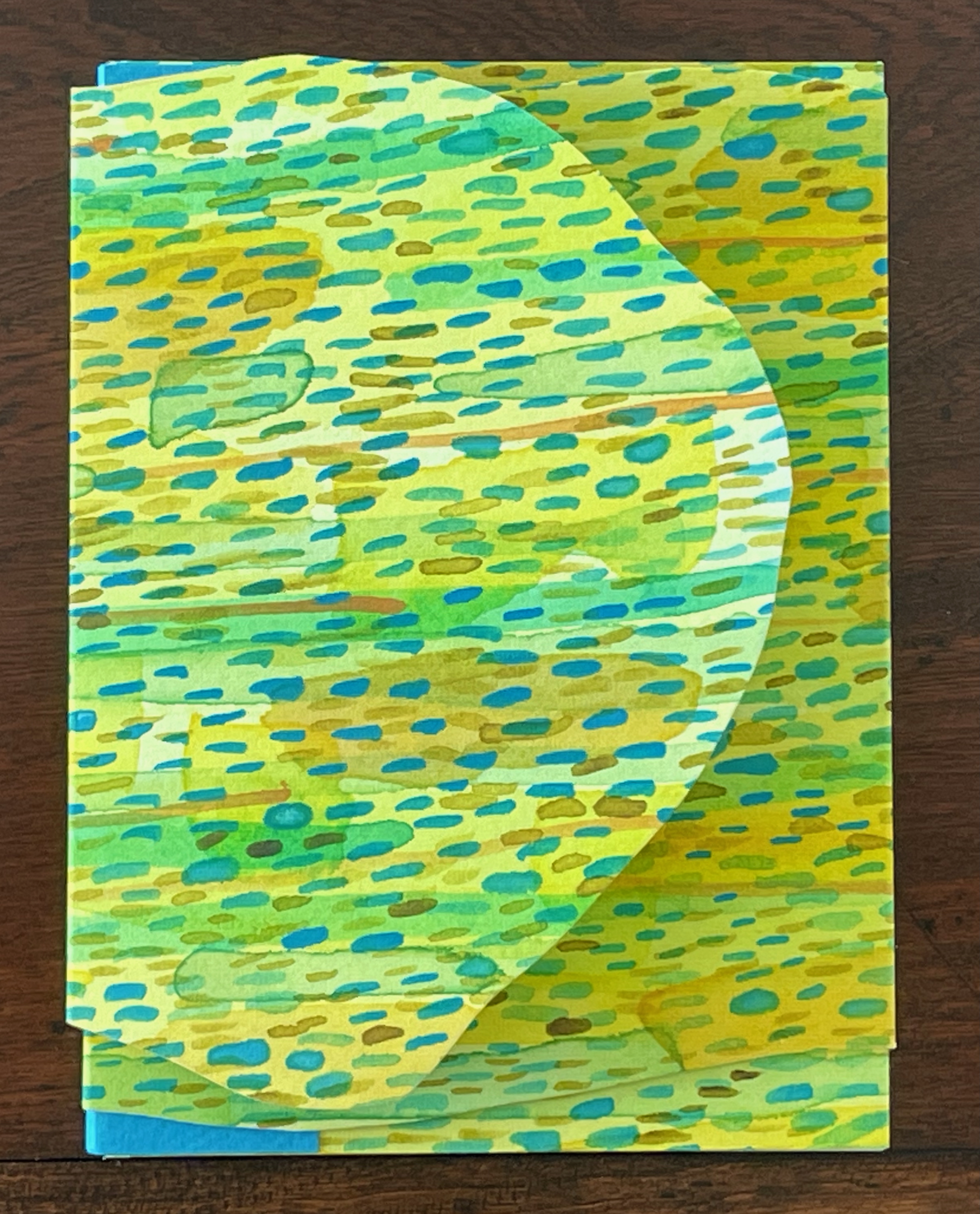 Colorful layered paper art featuring abstract patterns in green, blue, and yellow hues.