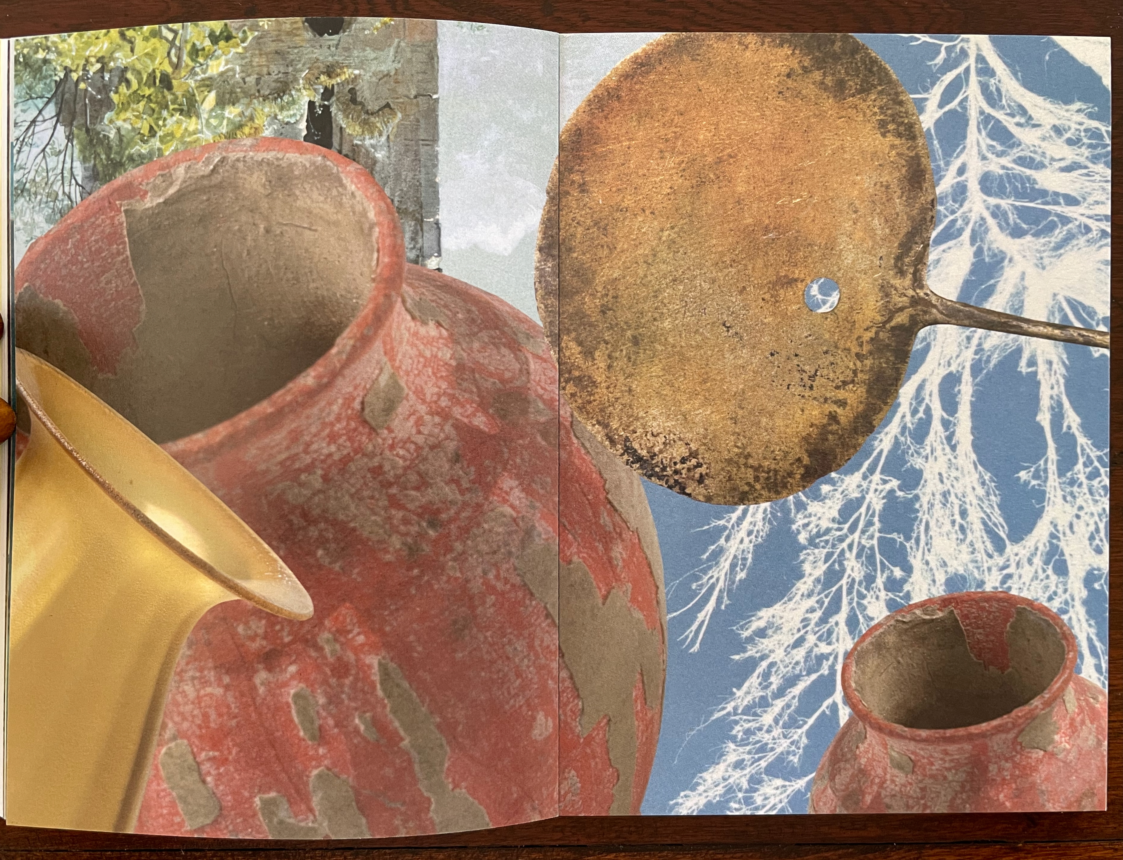Close-up of textured red pottery and a brass ladle against a blue background with white tree branches.