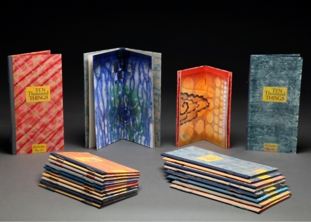 A collection of artistic books titled 'Ten Thousand Things' displayed in various colorful covers and opened pages, showcasing unique designs and patterns.