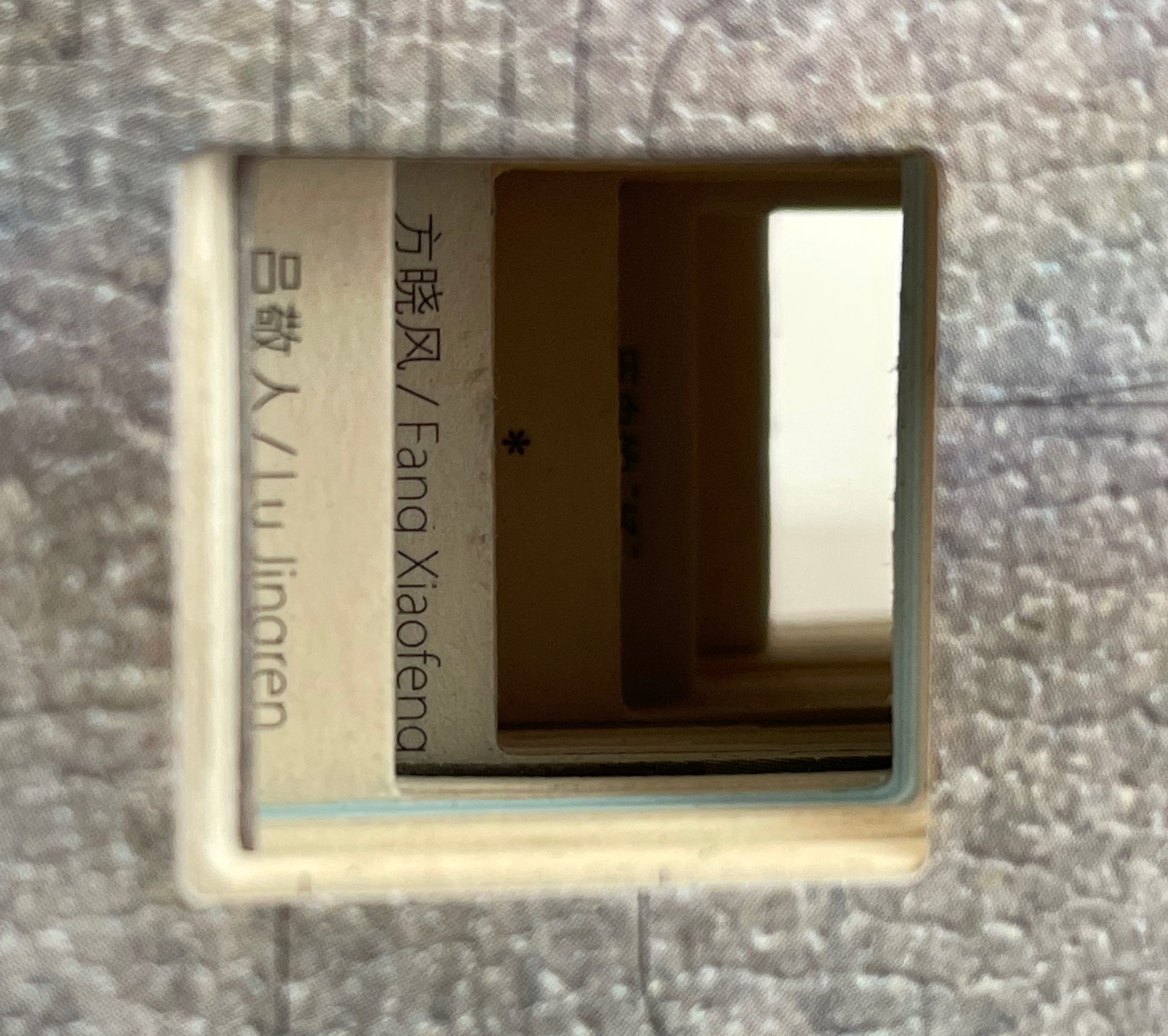 A close-up view of a square cutout in a book cover, revealing partially visible text in another language and a hint of a page behind it.