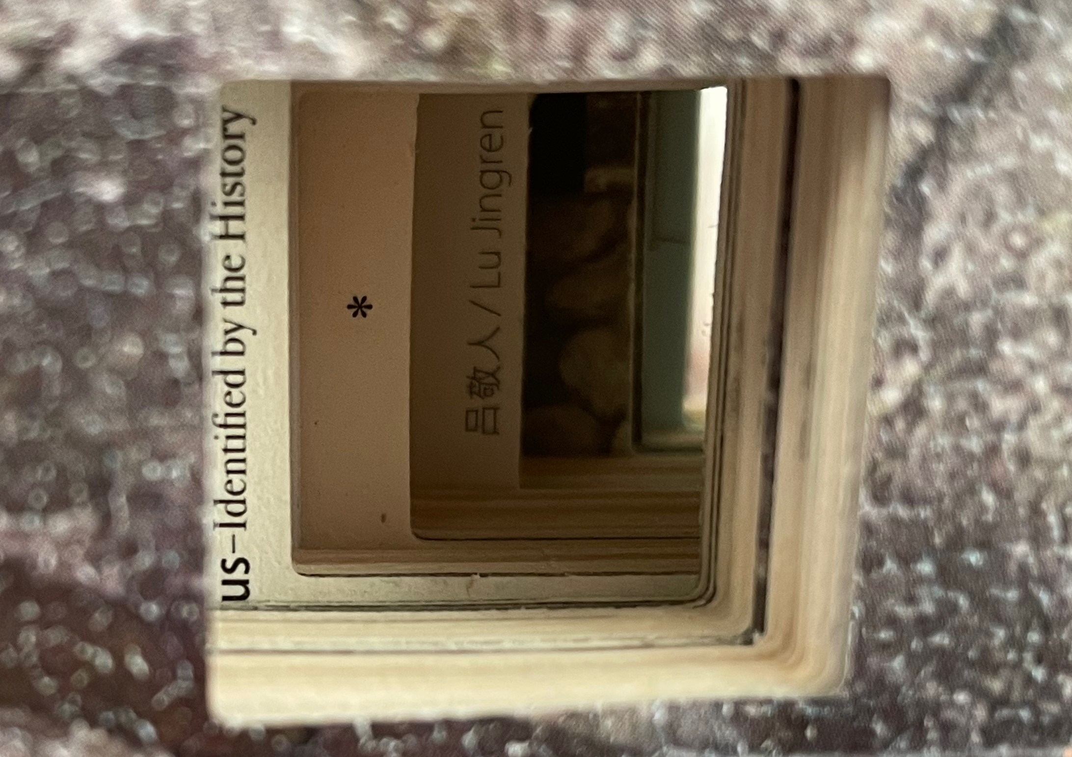 View through a layered cutout showcasing the text 'US - Identified by the History' alongside names, partially obscured by a textured background.