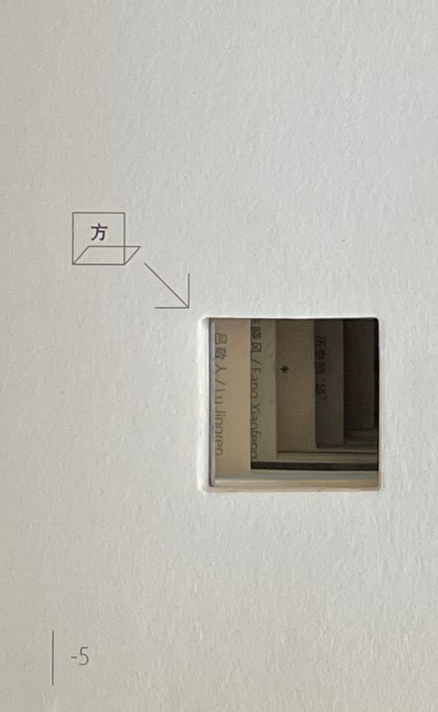 A close-up view of a cutout in a white page, revealing text written in Chinese from the pages behind it.