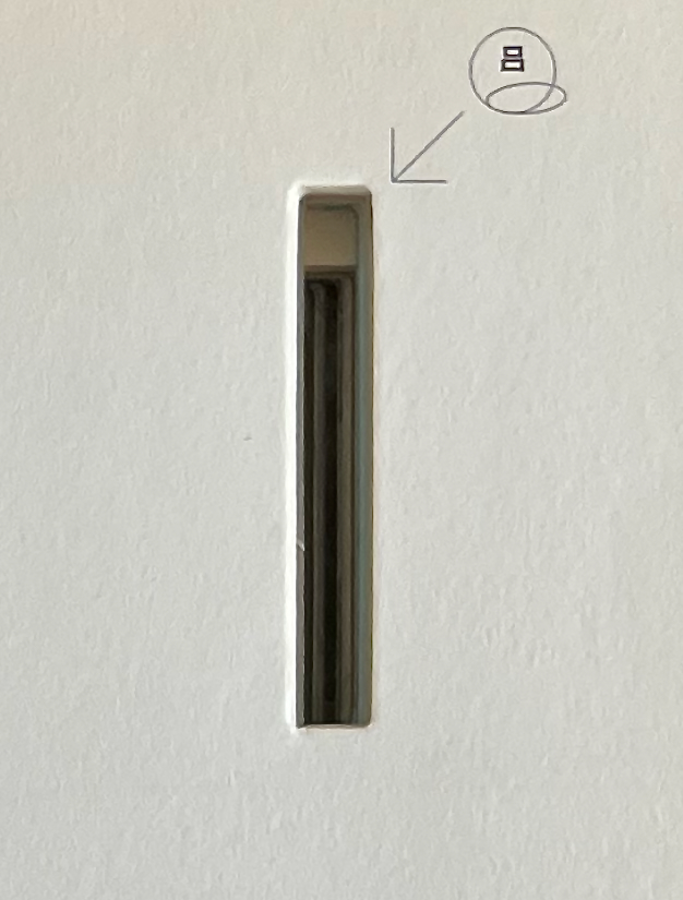 Close-up view of a narrow vertical slot on a white surface, with a small arrow pointing to it.