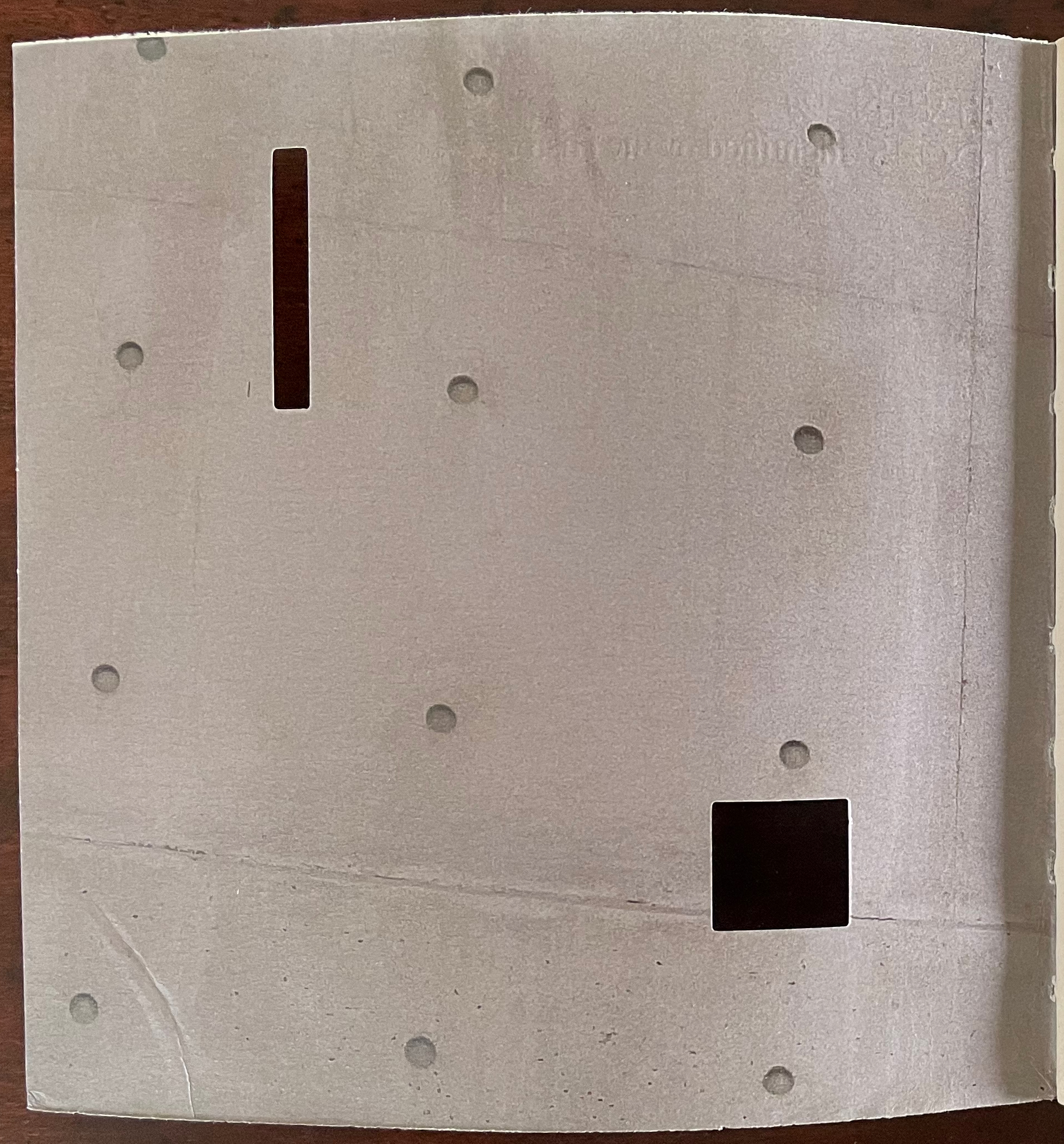 A light-colored, textured surface with several small holes and two cutouts, one rectangular and one square, visible on the surface.