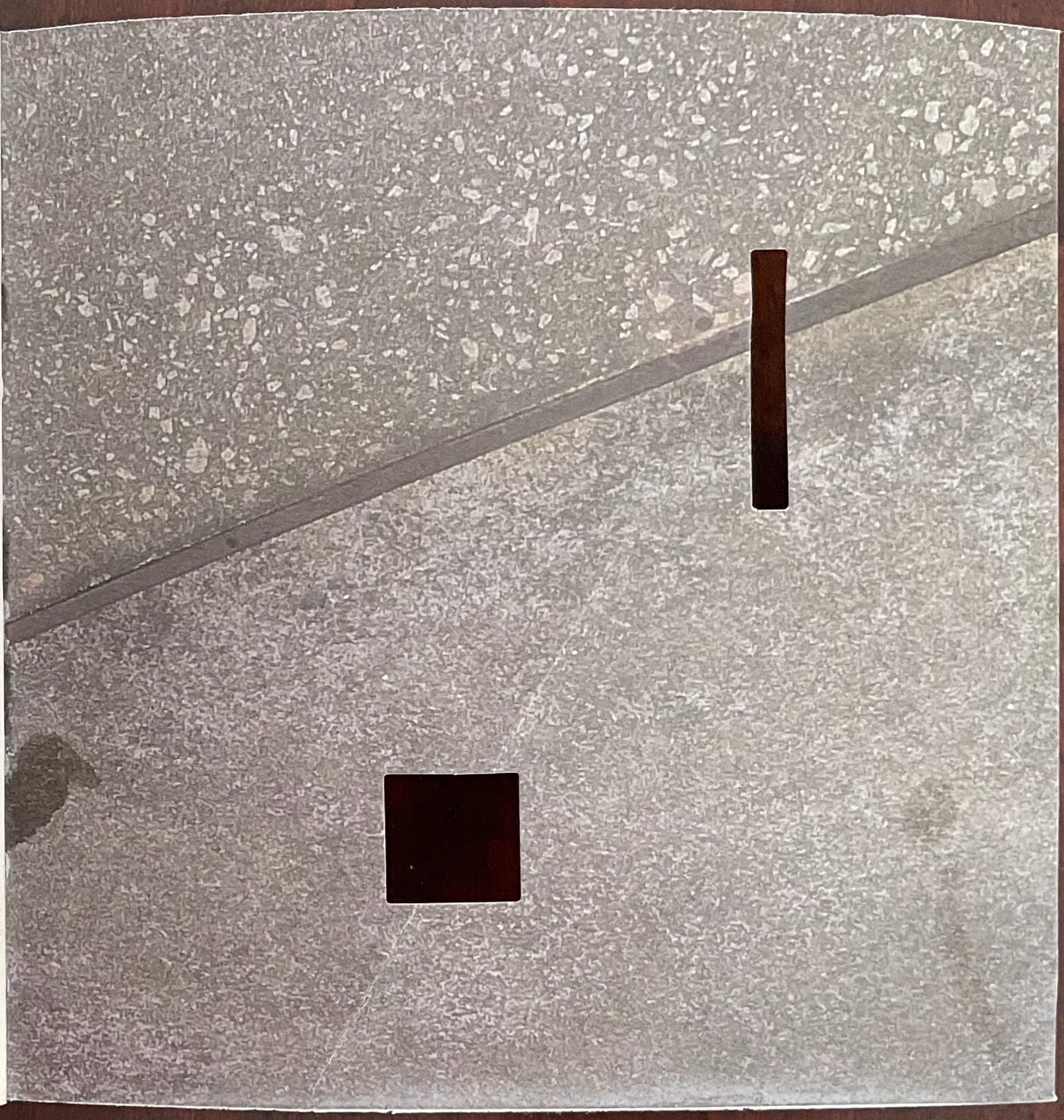 Abstract image featuring textured gray surfaces with two dark rectangular shapes positioned on the surface.