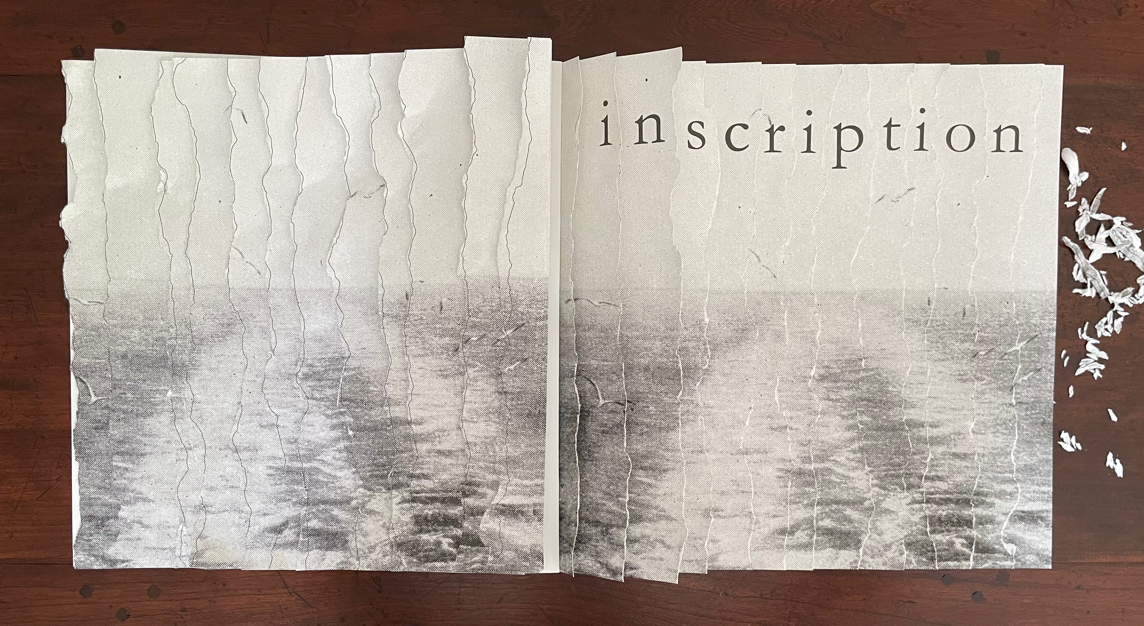 An open book with a textured, faded image of water on the pages, featuring the word 'inscription' elegantly displayed across the top.