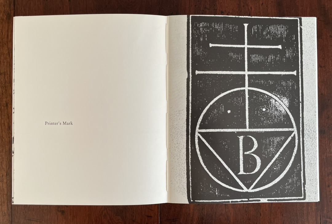 An open book displaying a page with the title 'Printer's Mark' and an illustration of a circular design featuring the letter 'B' and geometric shapes.