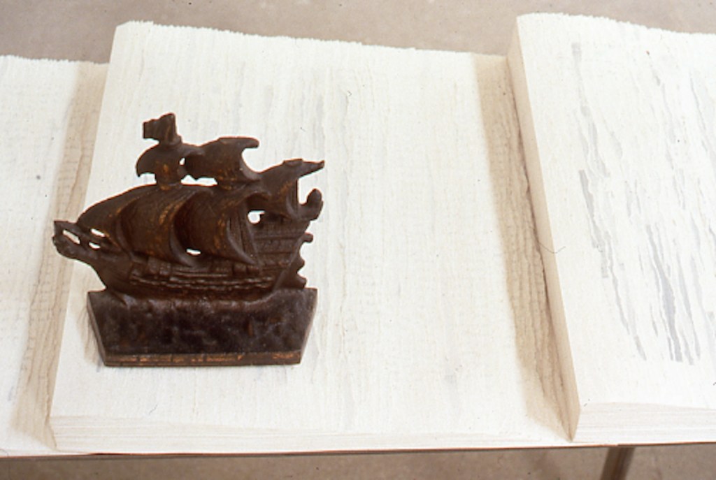 A small decorative ship sculpture made of cast iron, positioned on a white wooden surface with a textured grain.