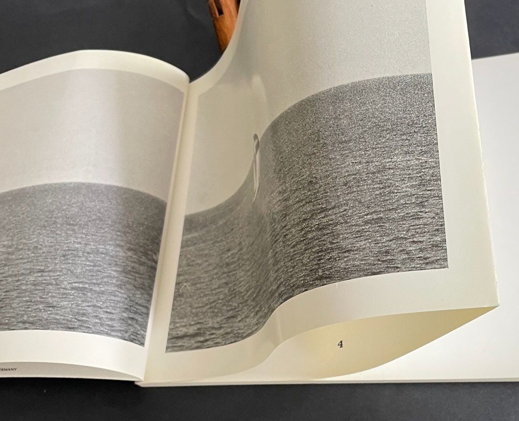 A close-up of an open book showing a black and white image of a solitary figure in a vast landscape, with pages partially turned.