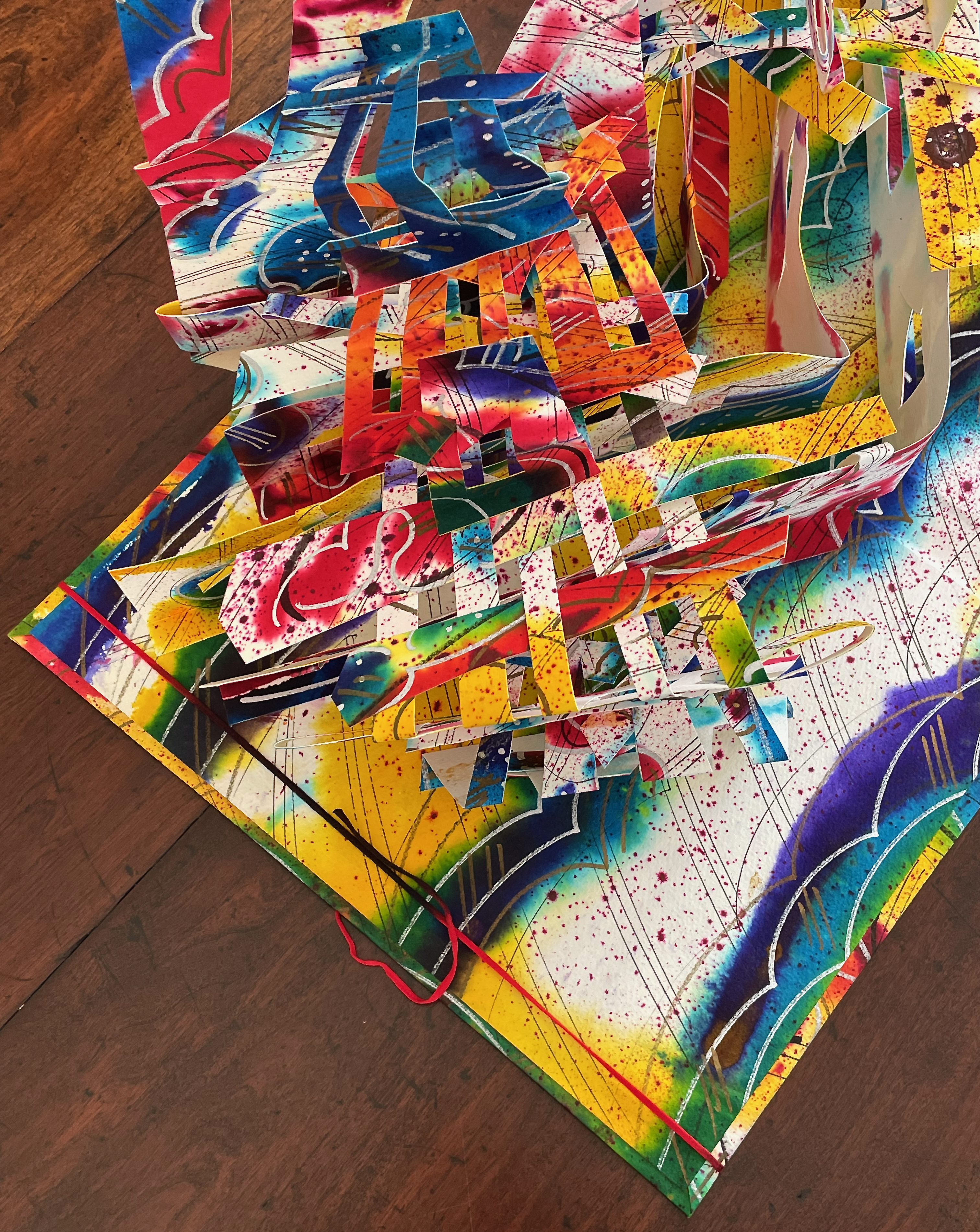 A vibrant, colorful 3D paper structure with various layers and shapes, set against a bright, splatter-painted background.