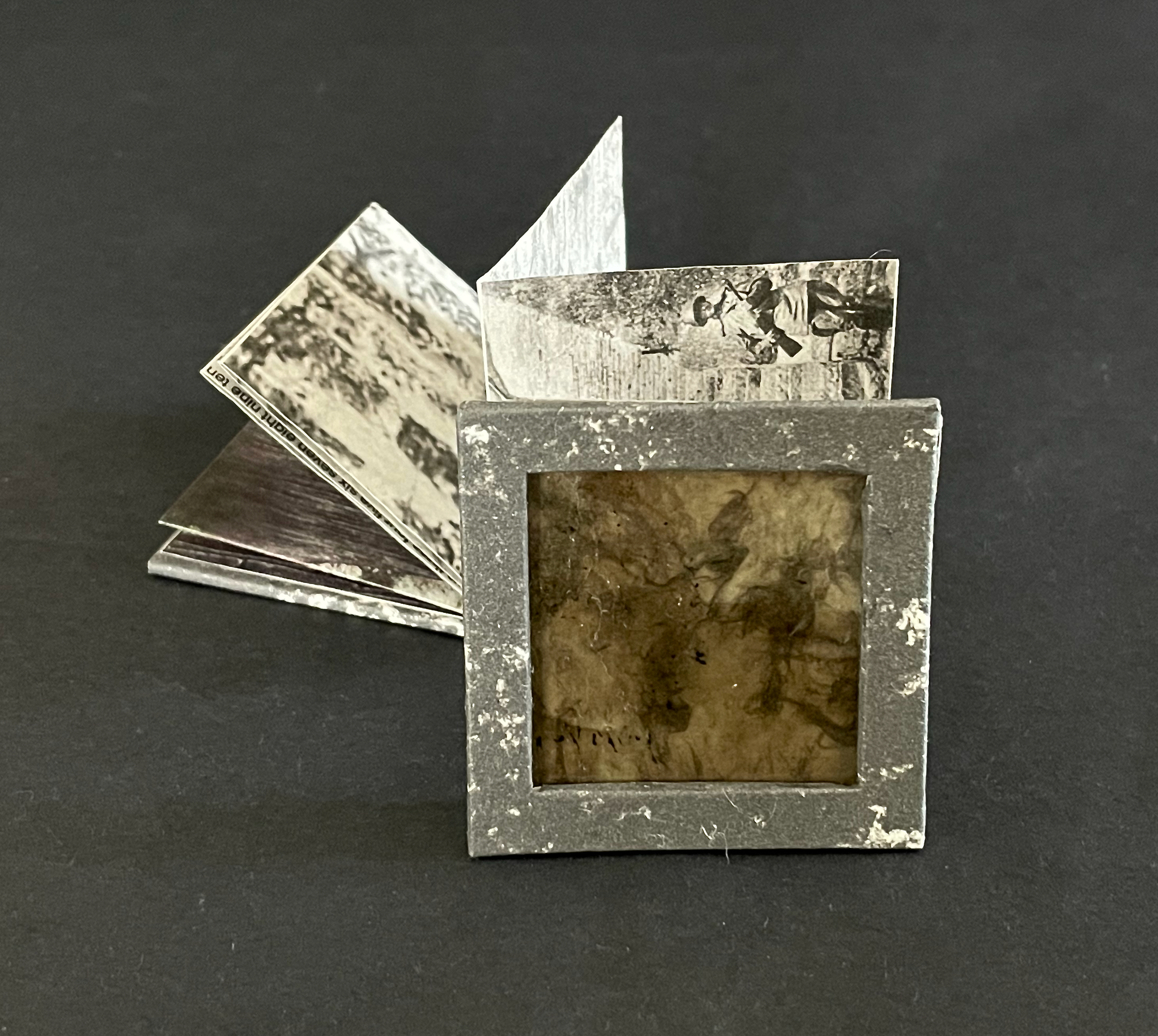 An open vintage photo album featuring black and white photographs, with a square frame at the front displaying a textured surface.