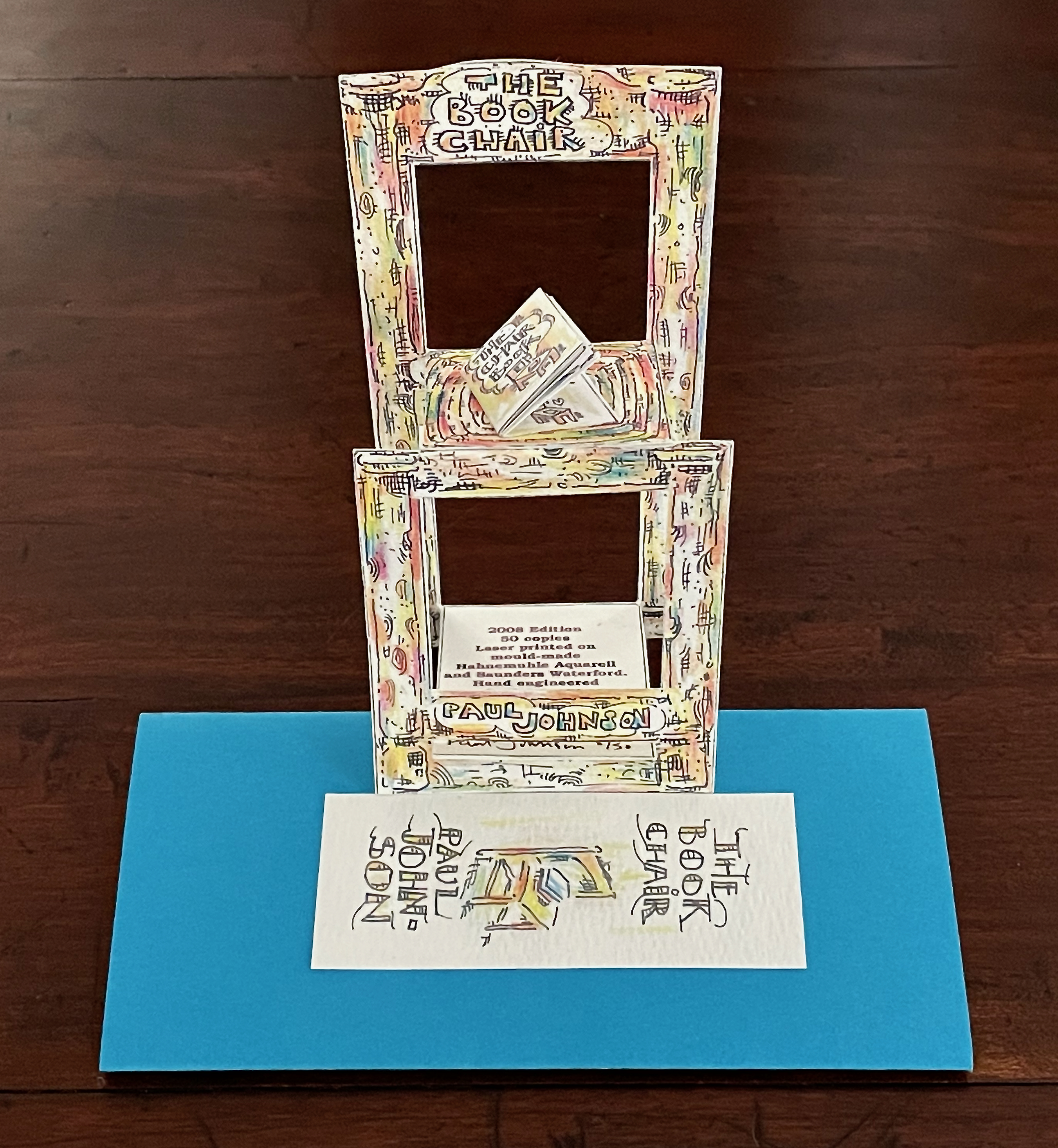 A colorful pop-up book titled 'The Book Chair' by Paul Johnson, displaying a layered structure with frames and a blue background.