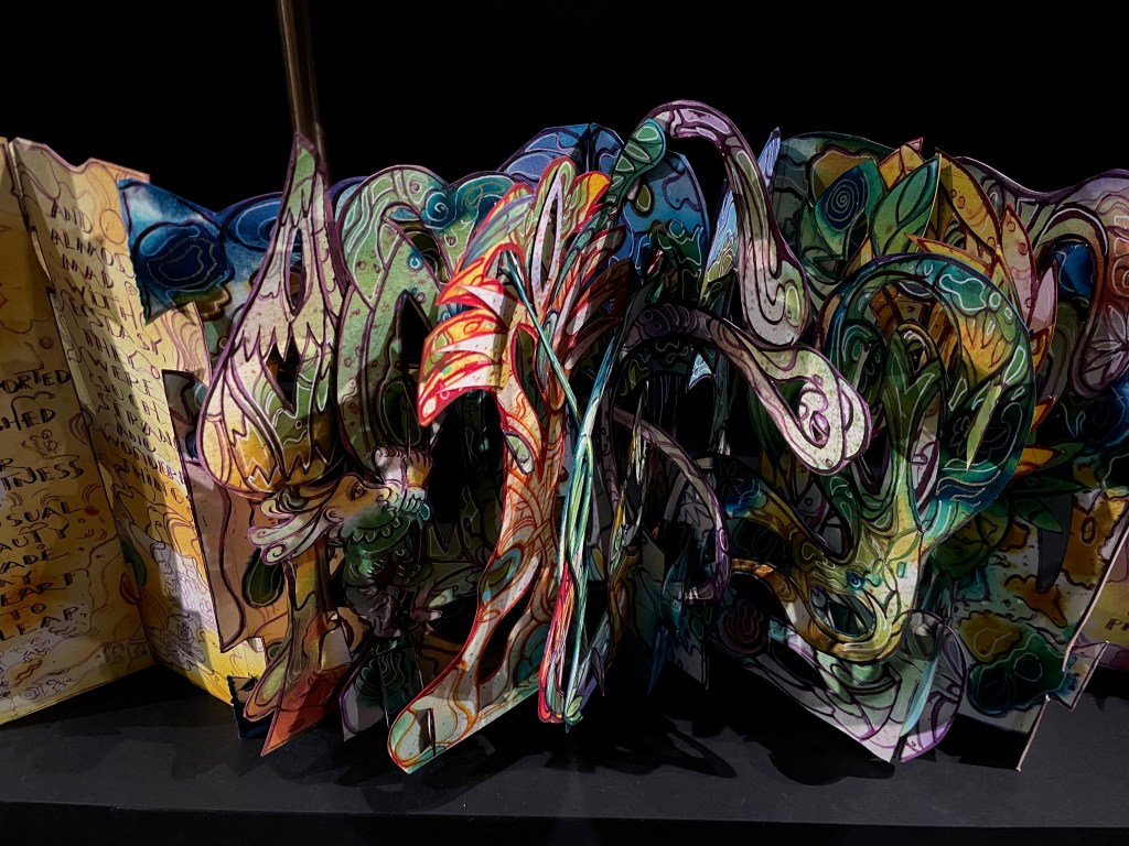 A vibrant pop-up book opened to reveal intricate, colorful illustrations with swirling designs and fantastical creatures.