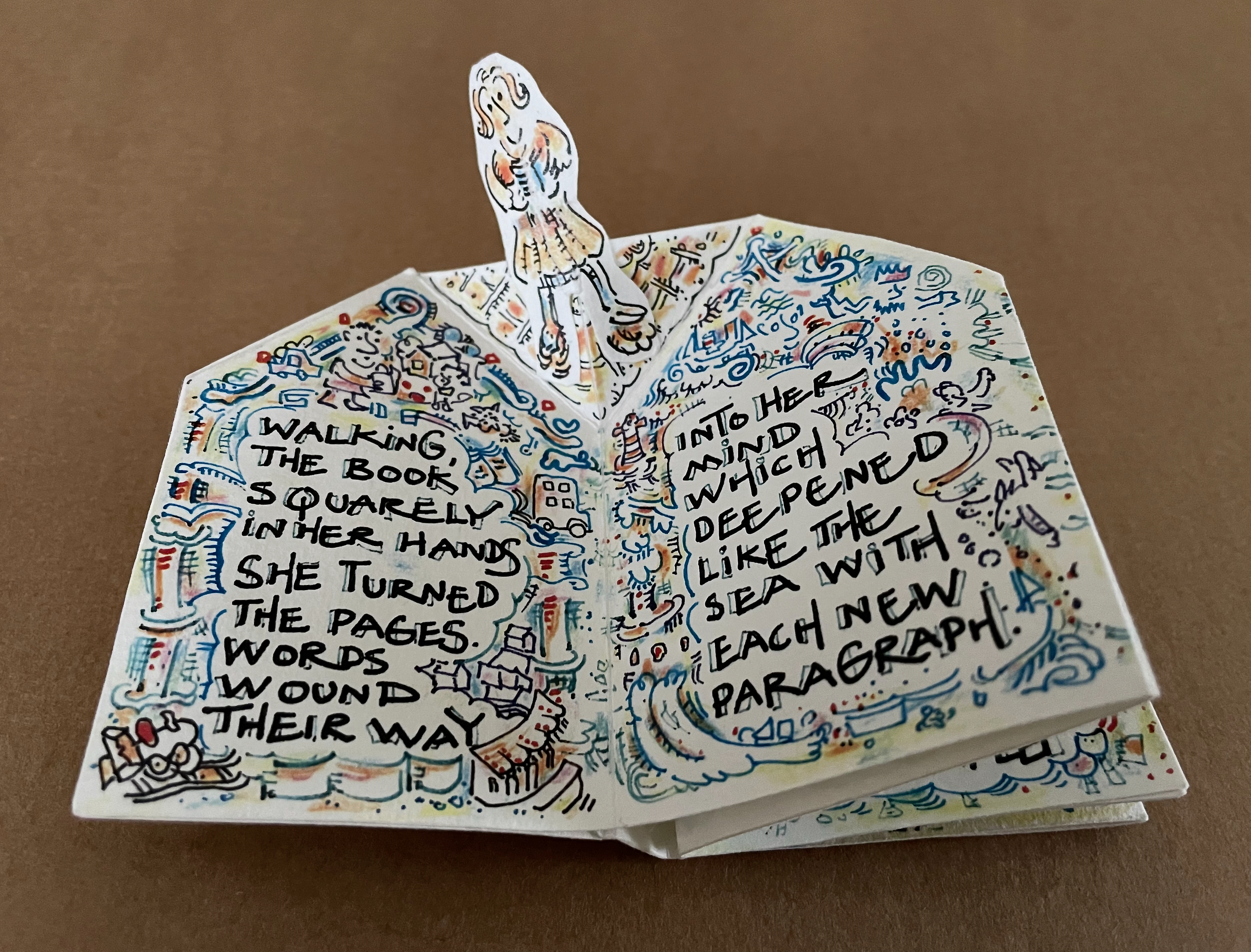 A pop-up book featuring a character holding a book, with colorful illustrations surrounding text that describes her experience of reading and exploring new thoughts with each paragraph.