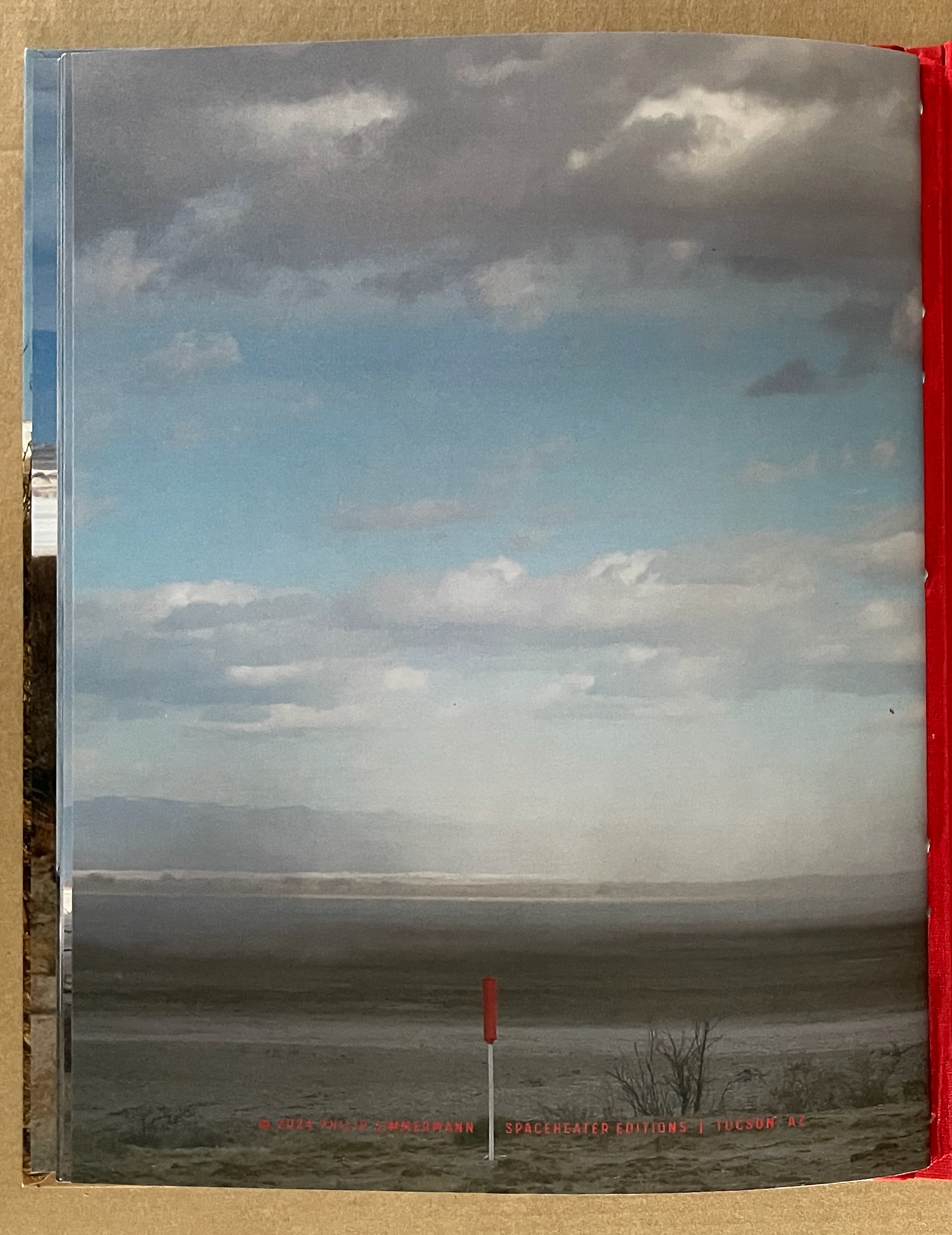 Landscape image featuring a vast, arid terrain under a cloudy sky, with a prominent red pole in the foreground.