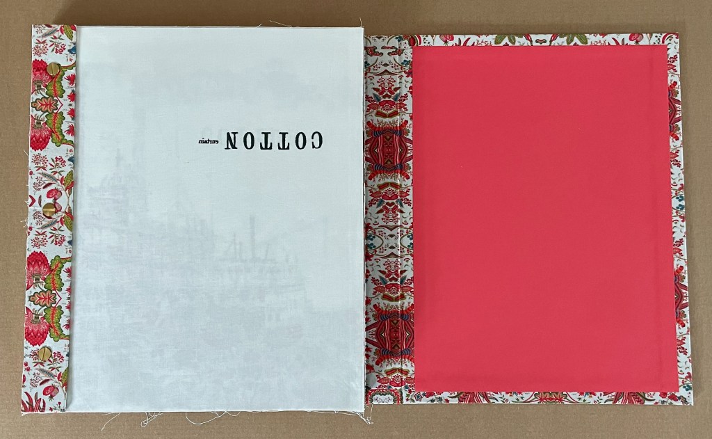 Open hardcover book with decorative floral spine, featuring the text 'COTTON' printed upside down on the left page, and a plain coral right page.