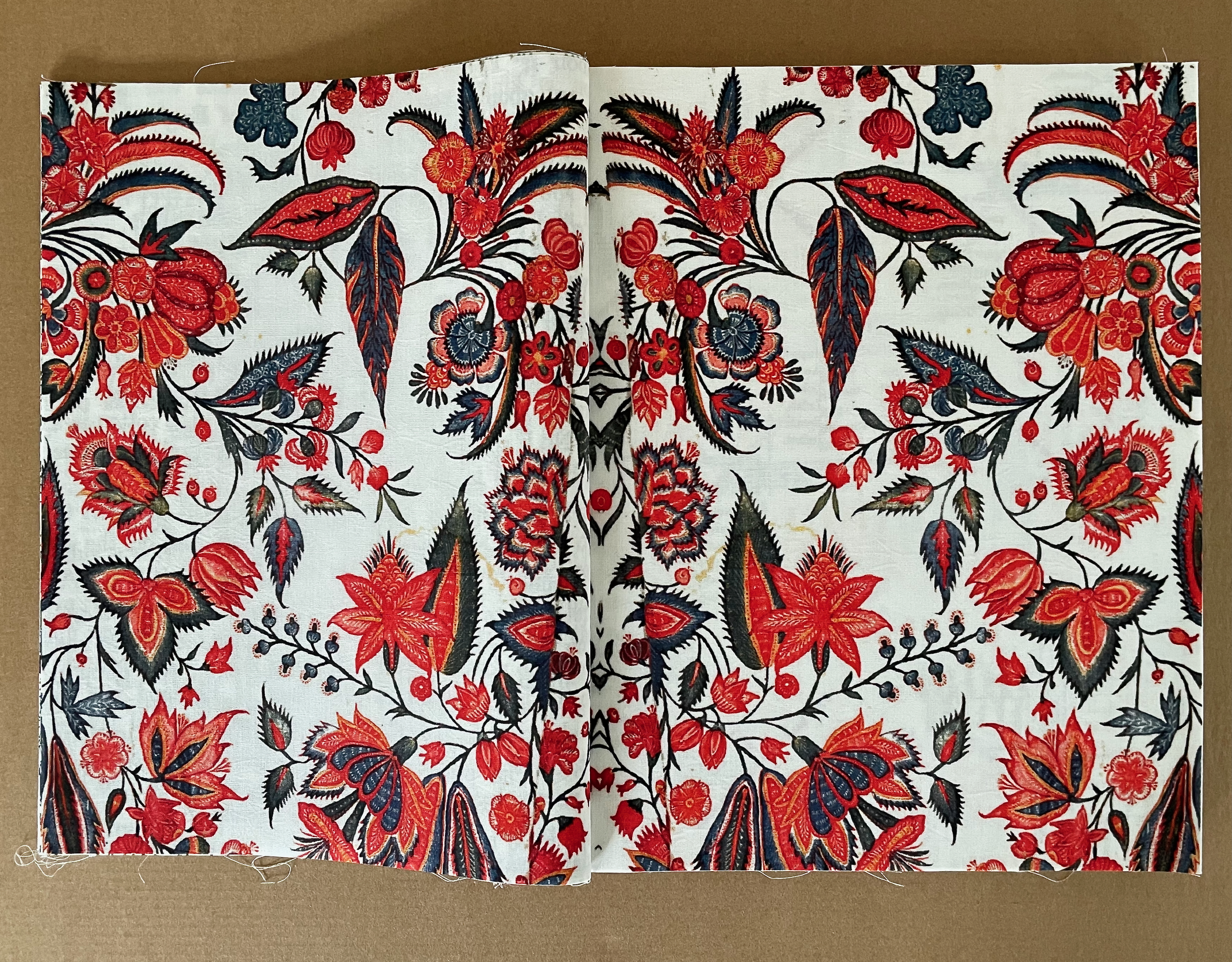 A vibrant textile pattern featuring intricate floral designs in red, blue, and black on a white background.