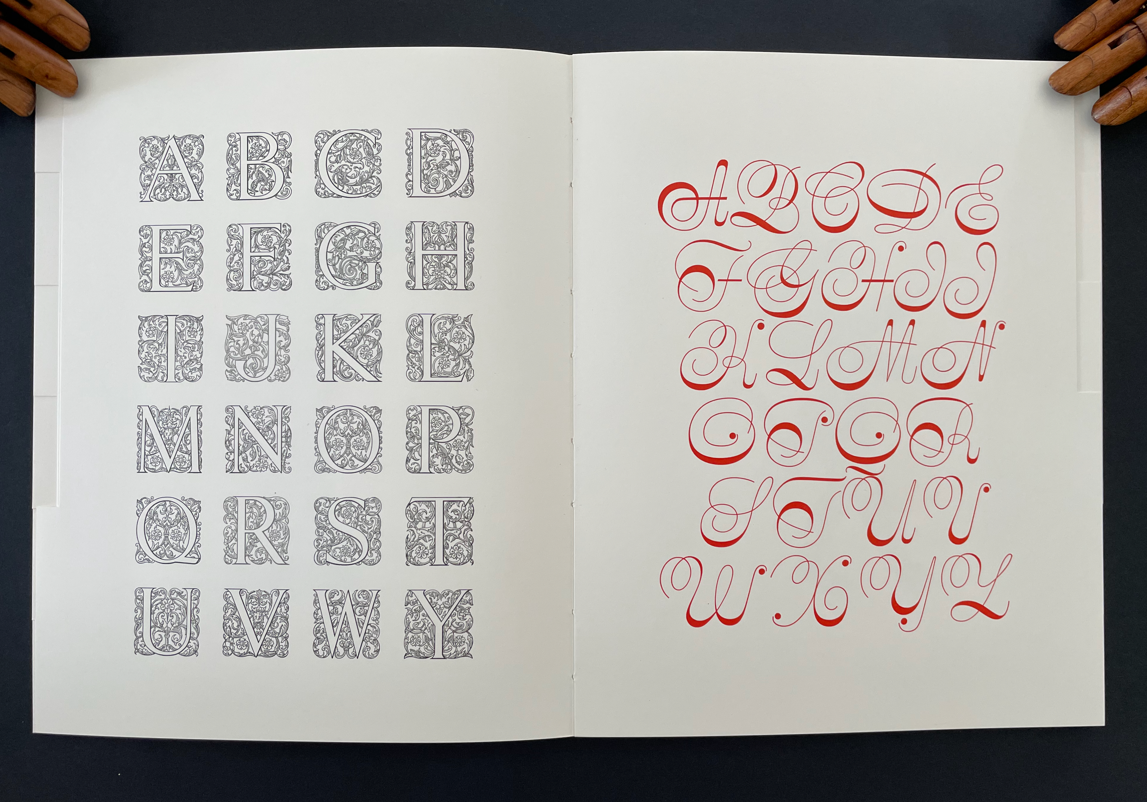 Stylized alphabet letters in ornate designs on two pages, with left side featuring decorative black and white letters and right side showcasing elegant red cursive letters.