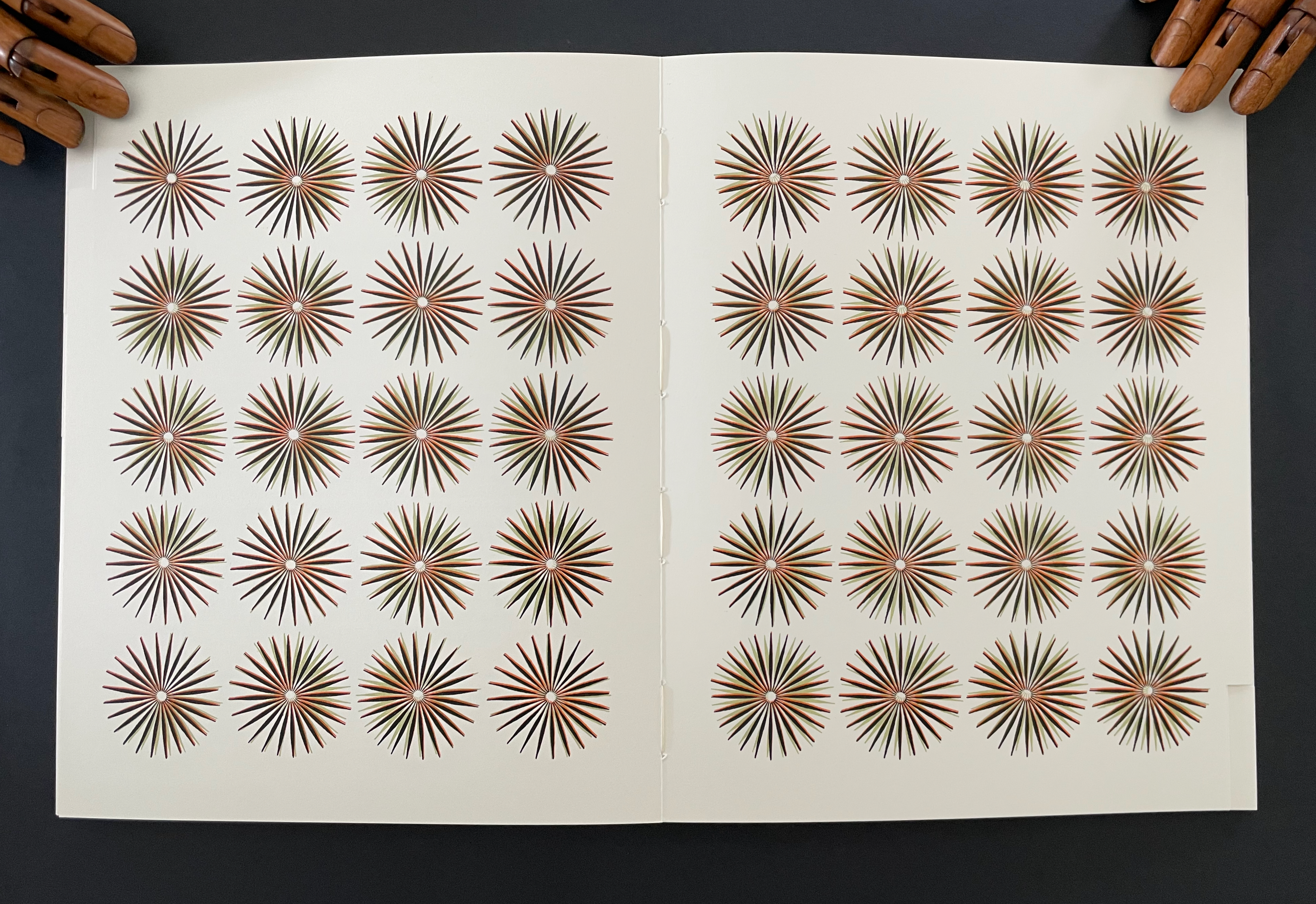 Opened book page displaying a grid of starburst designs with varying colors, arranged in four rows and five columns.
