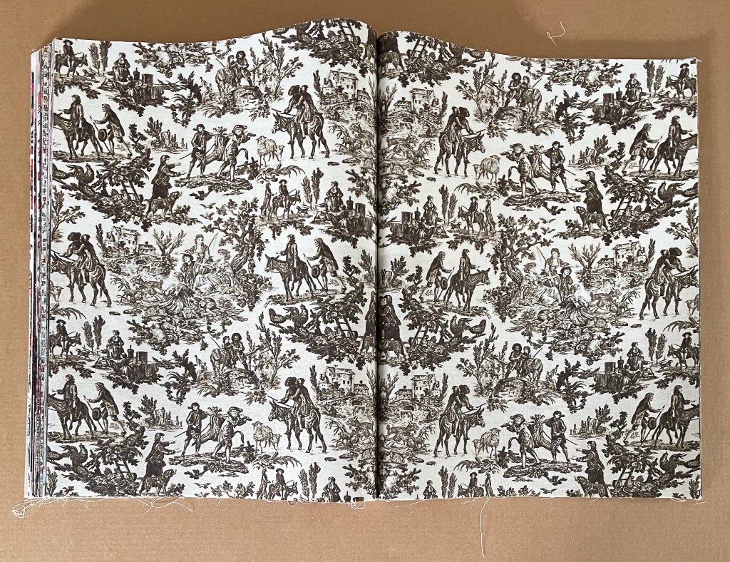 Open book displaying a printed fabric design featuring intricate illustrations of people, horses, and nature in a black and white pattern.