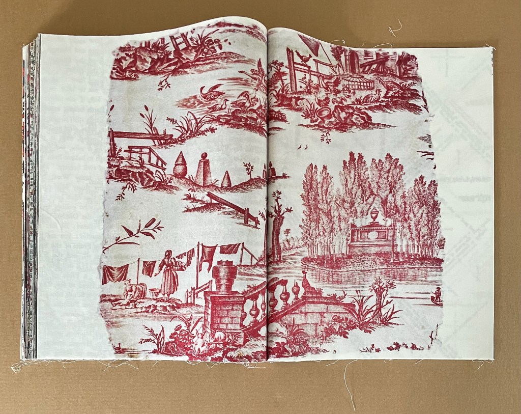 Open book displaying red and white toile pattern featuring pastoral scenes, including trees, gardens, and figures engaged in daily activities.