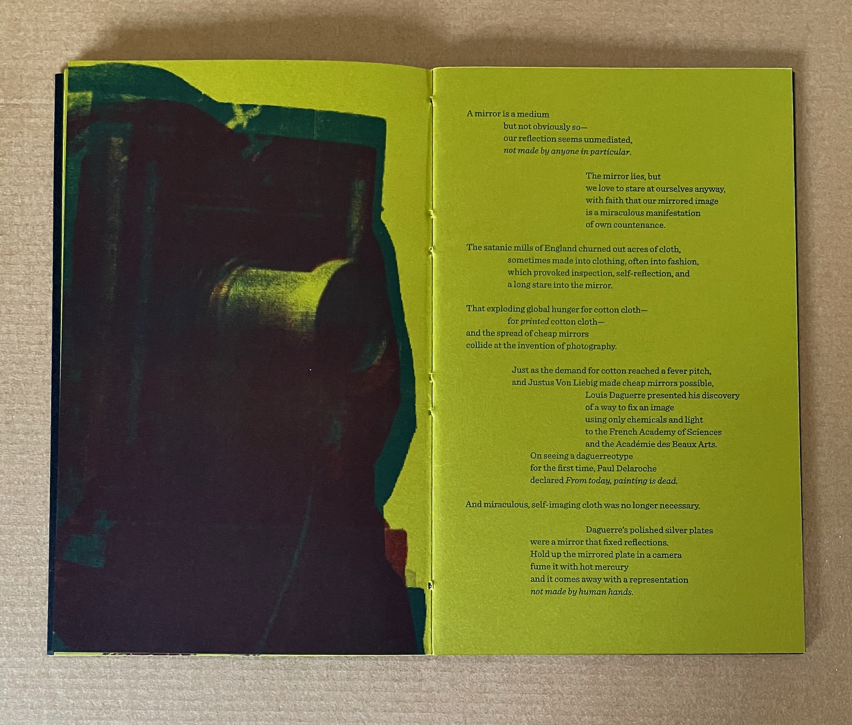 An open book featuring a two-page spread with a colorful abstract background, combining shades of yellow and dark colors. The left page contains an image of a mechanical device or camera, while the right page features text discussing the relationship between mirrors, photography, and cotton production.