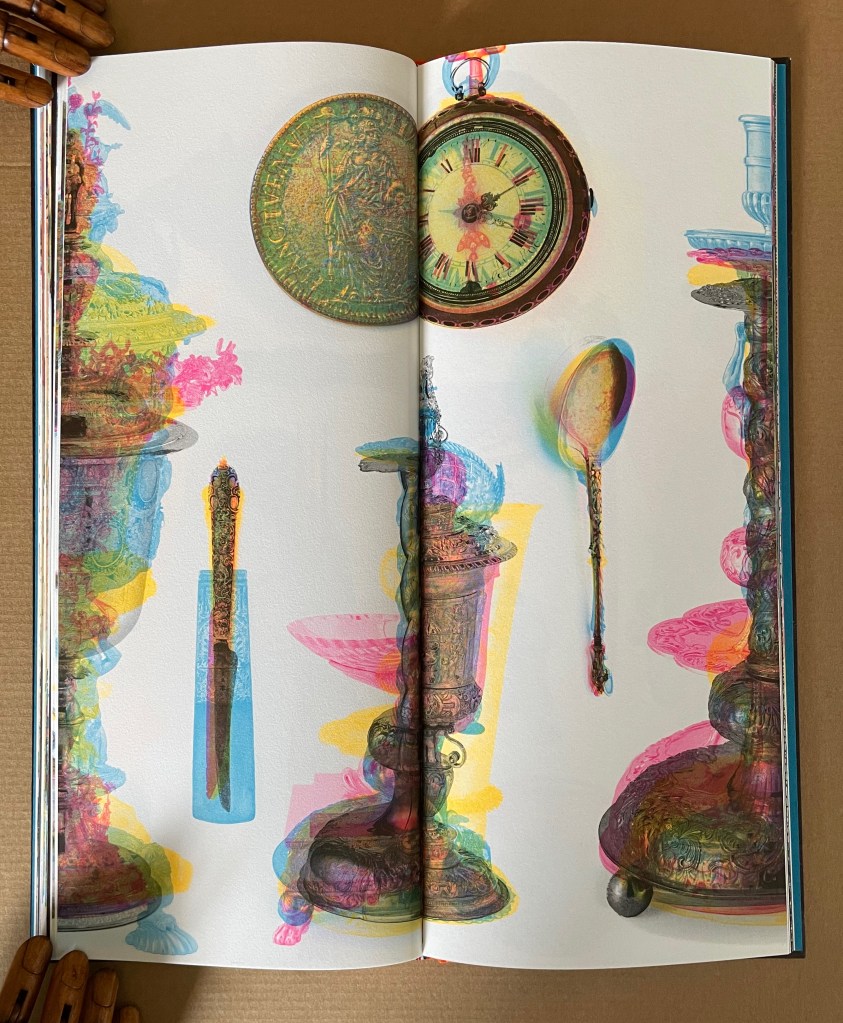 An artistic display of vintage objects including a clock, spoon, and decorative pieces, presented in vibrant colors and layered transparencies across the pages of a book.