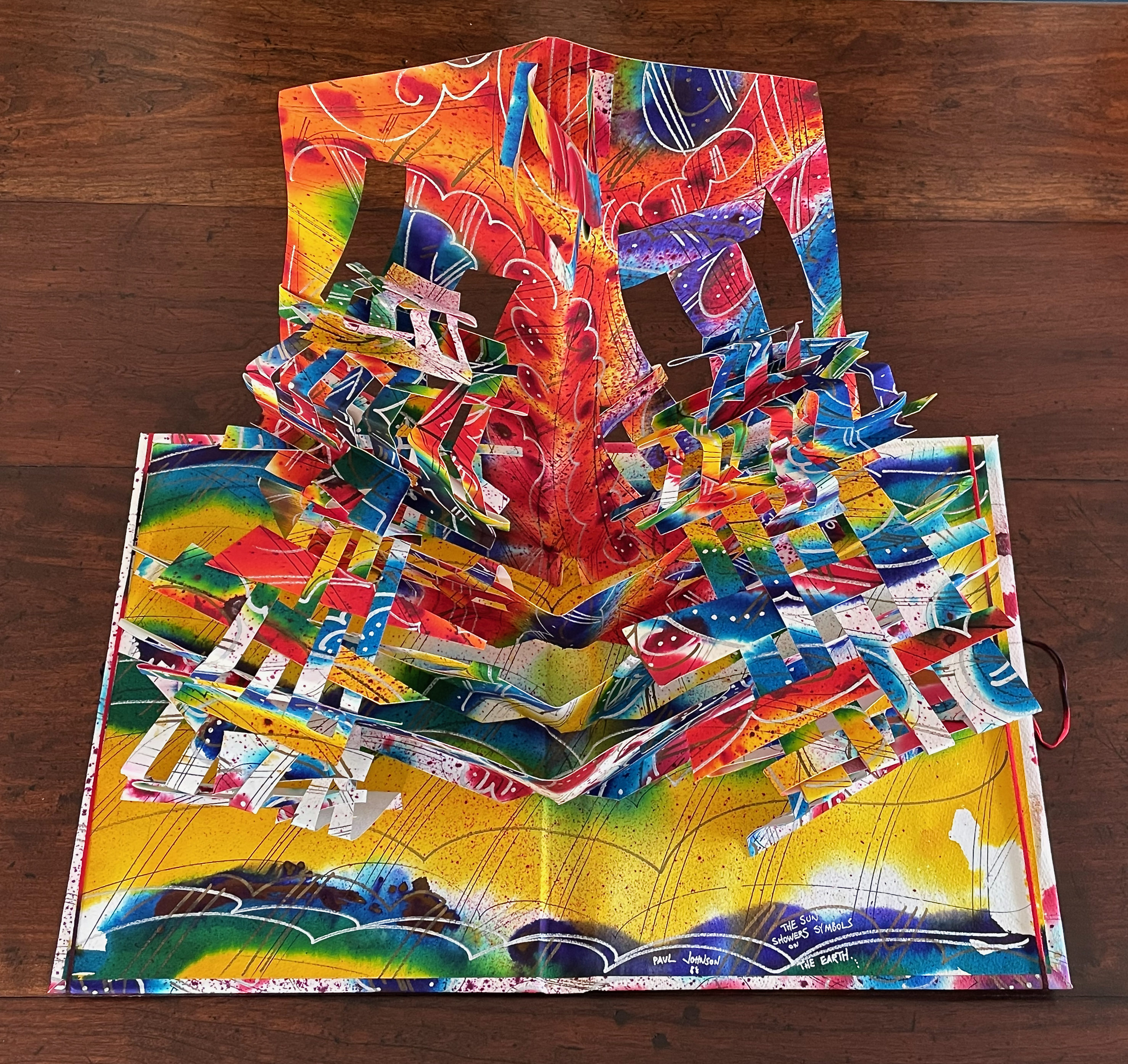 A vibrant pop-up book with intricate paper art, featuring an explosion of colors and layered designs, set against a colorful background.