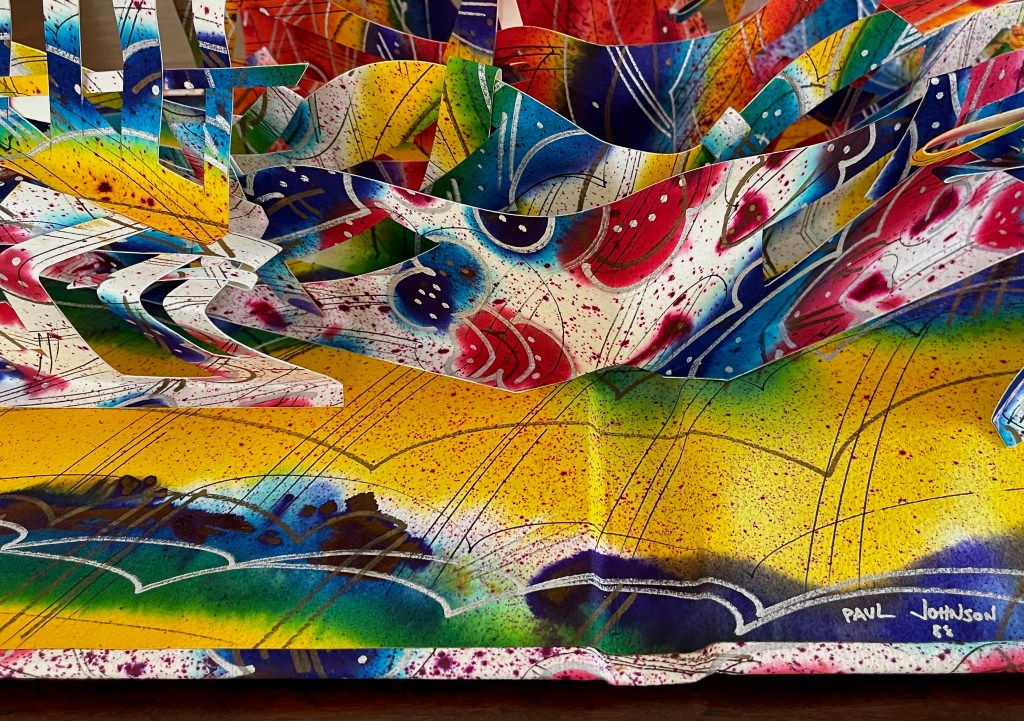 A colorful pop-up art display featuring vivid patterns and abstract designs in blue, yellow, red, and green, with intricate layers and textures.