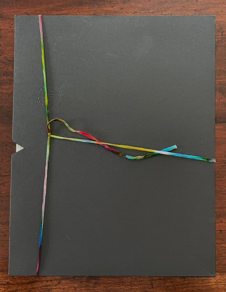 A closed black folder tied with colorful ribbon on a wooden surface.