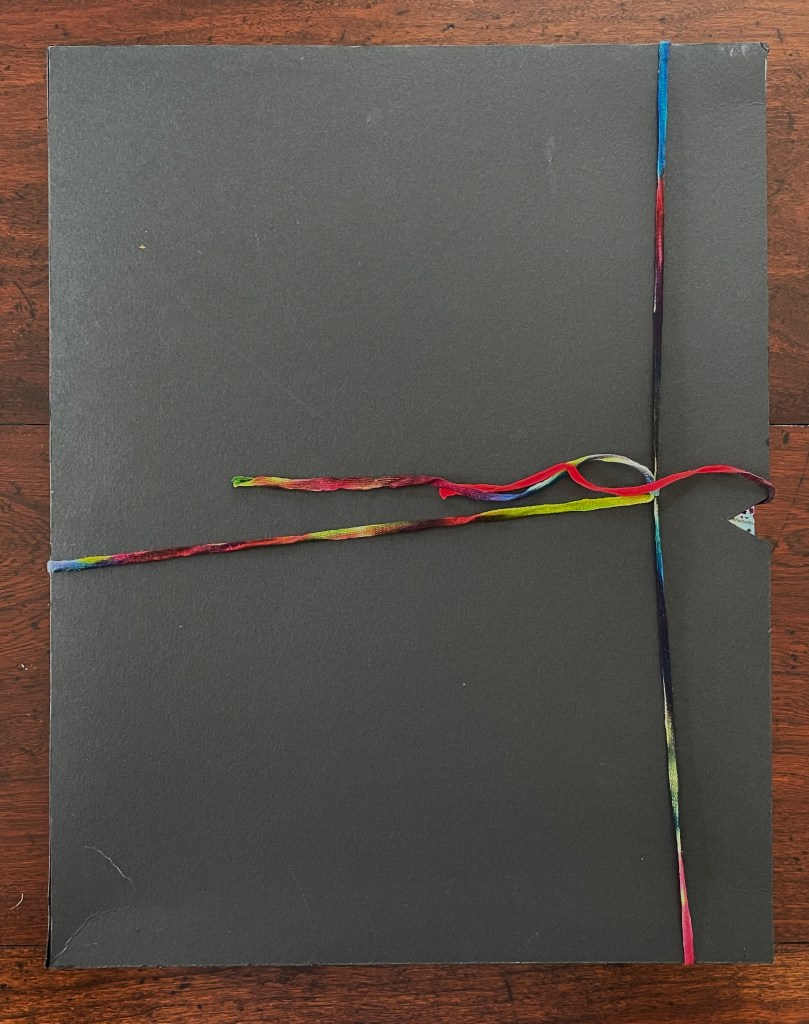 A closed black folder tied with a colorful ribbon, placed on a wooden surface.
