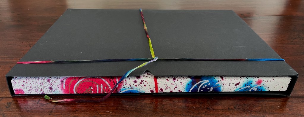 A closed book with a black cover, wrapped with a colorful, multi-stranded ribbon. The book's edges feature vibrant, abstract designs in pink, blue, and white.