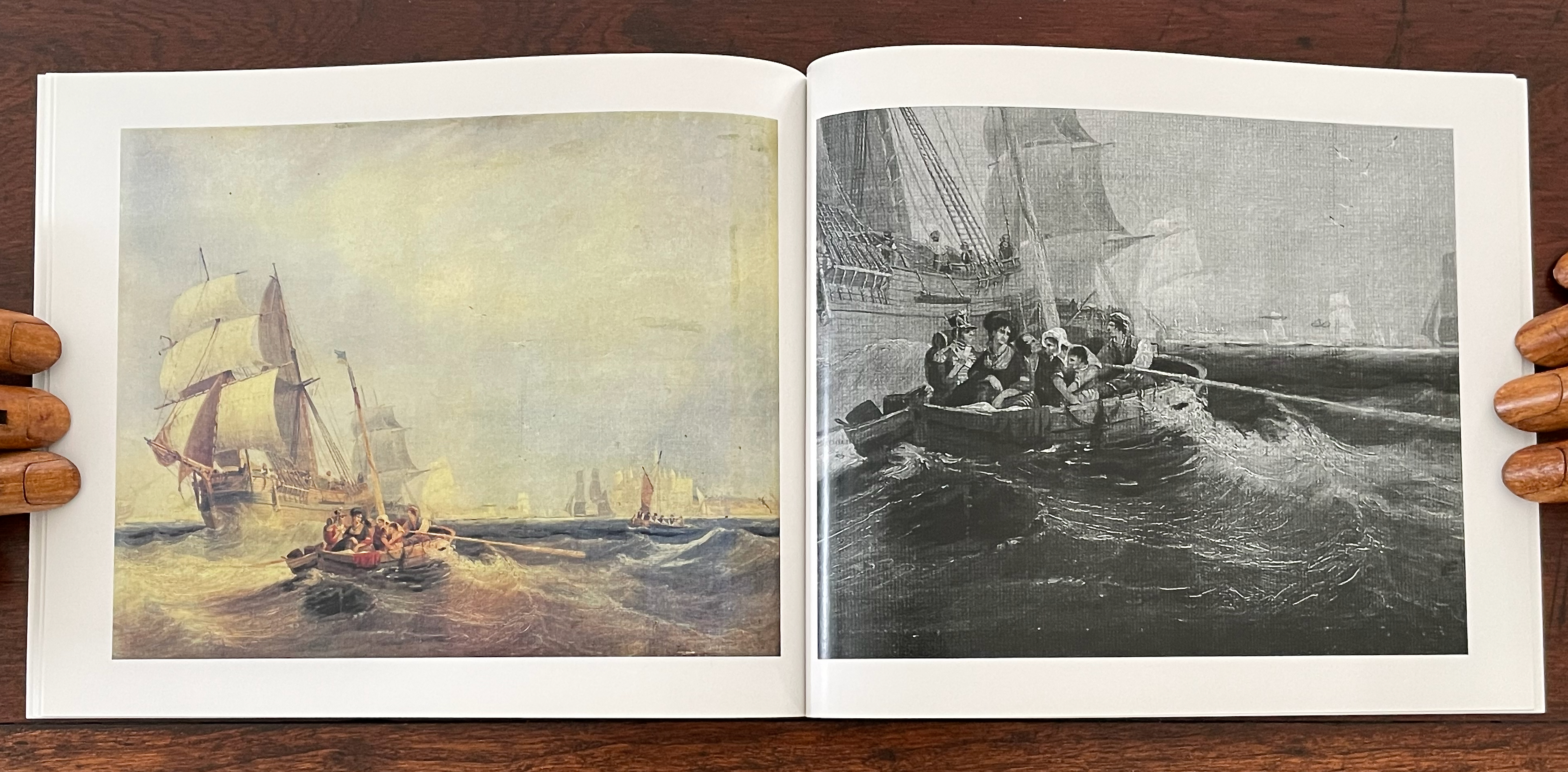 An open book featuring two pages with paintings of maritime scenes; the left page shows a colorful image of sailing ships on calm waters, while the right page displays a black-and-white illustration of a small boat with several people navigating through rough seas.