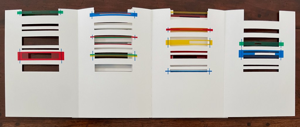 A collection of white sheets of paper with various horizontal slits and colored strips inserted, displayed on a wooden surface.