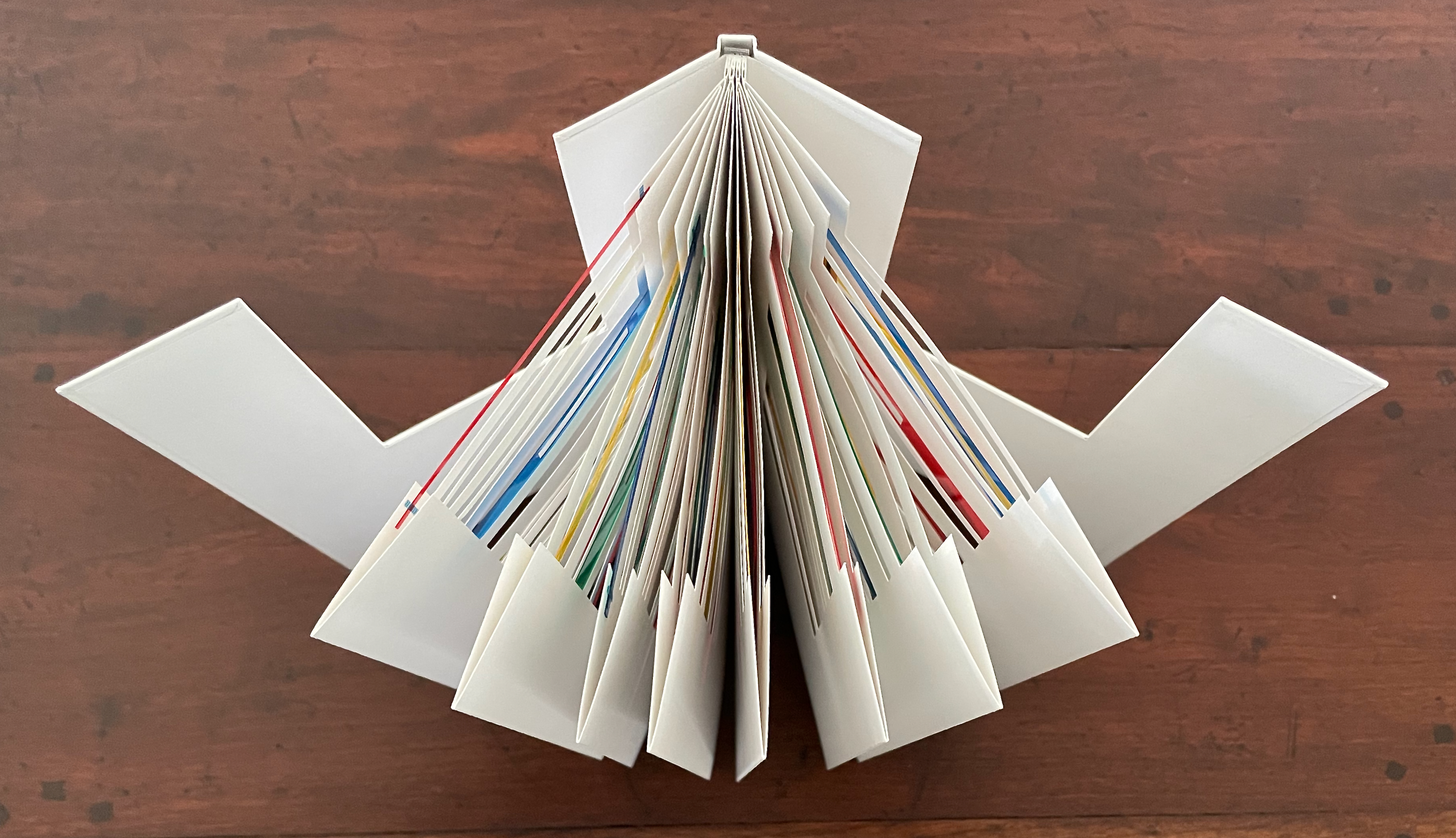 An open book standing upright, displaying colorful pages fanned out in an arch on a wooden surface.