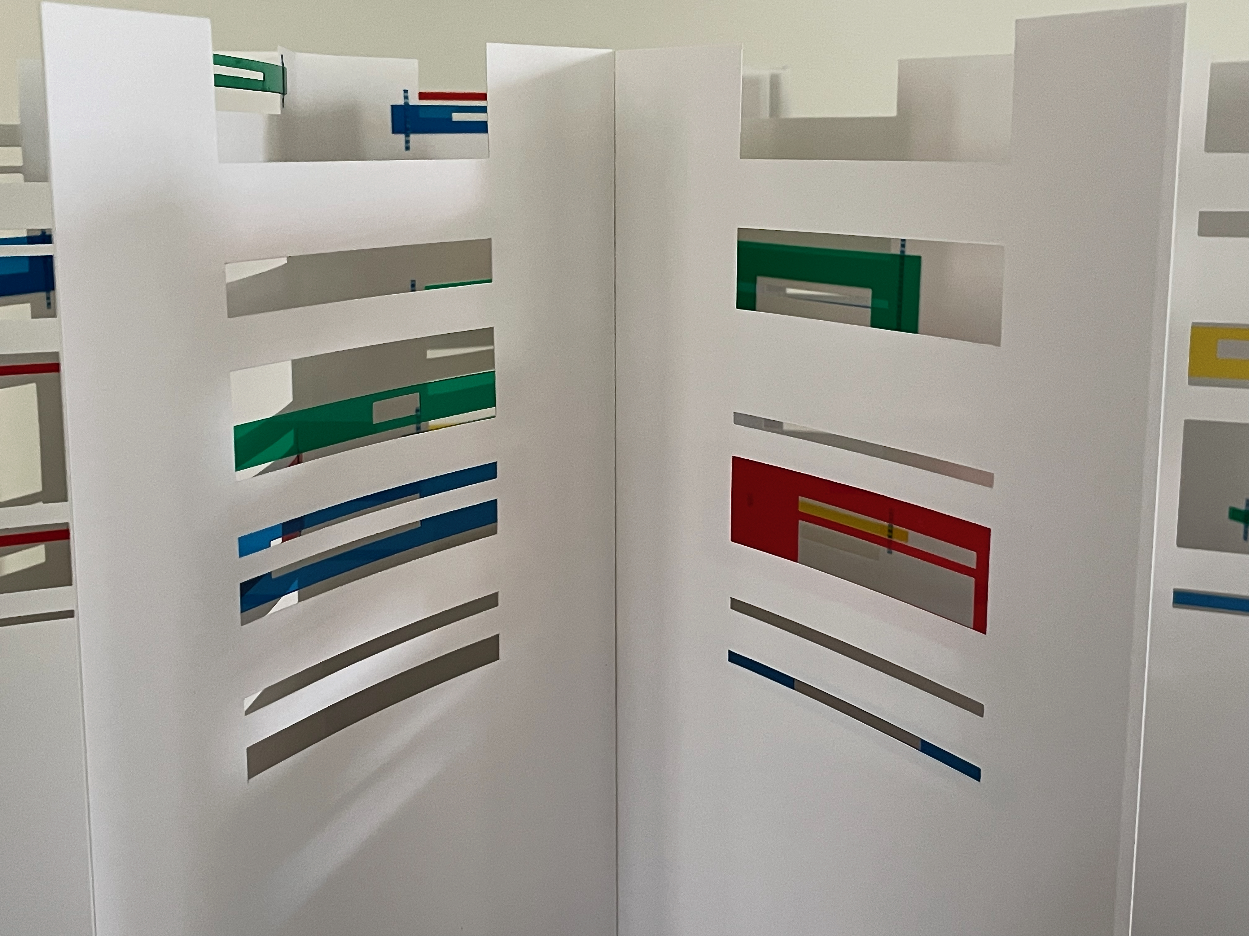 A close-up view of a white architectural model featuring cut-out sections and colorful layered elements in red, green, blue, and yellow.