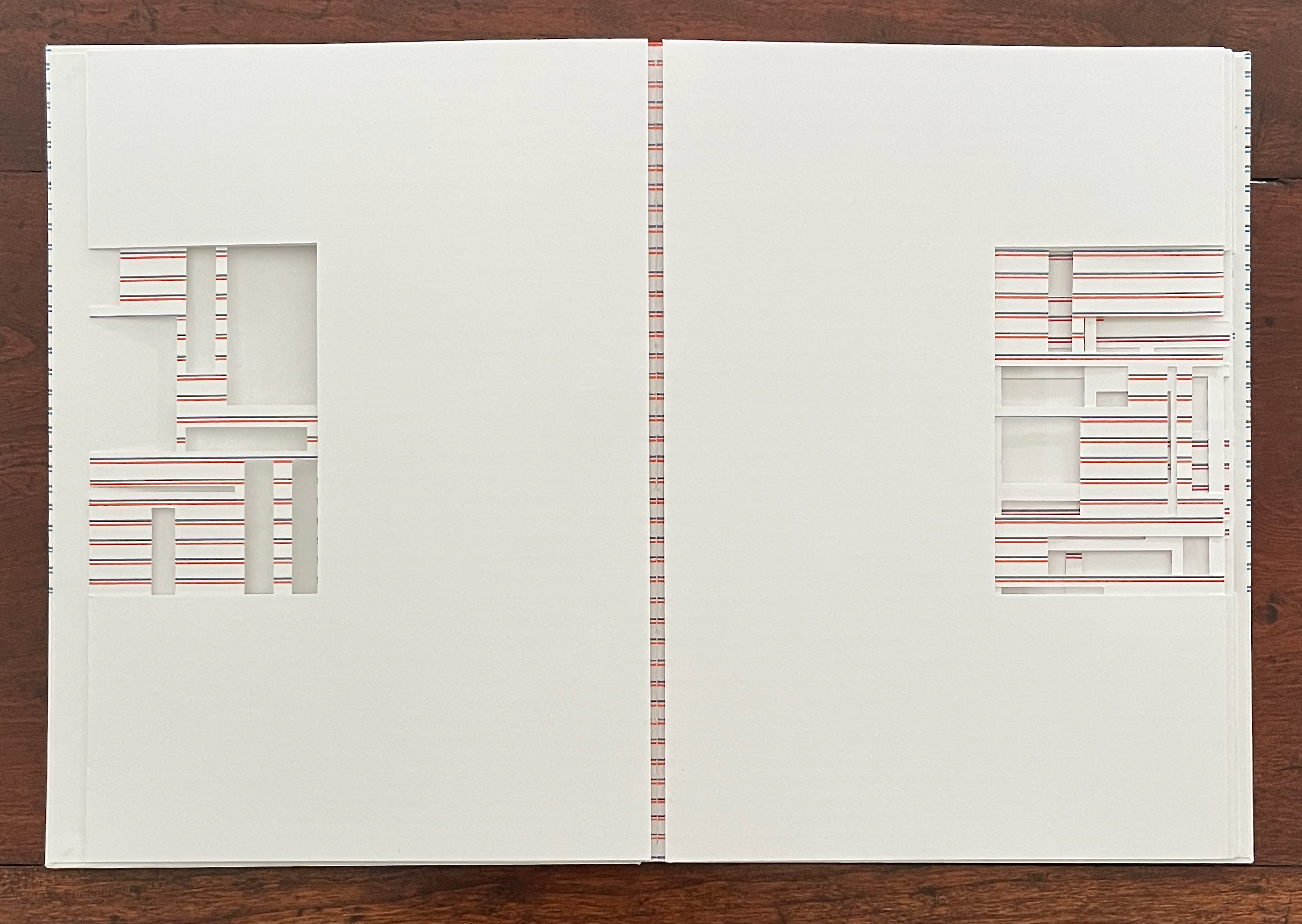 An open book with two white pages featuring intricate cut-out designs on both sides, revealing red and white striped patterns beneath.