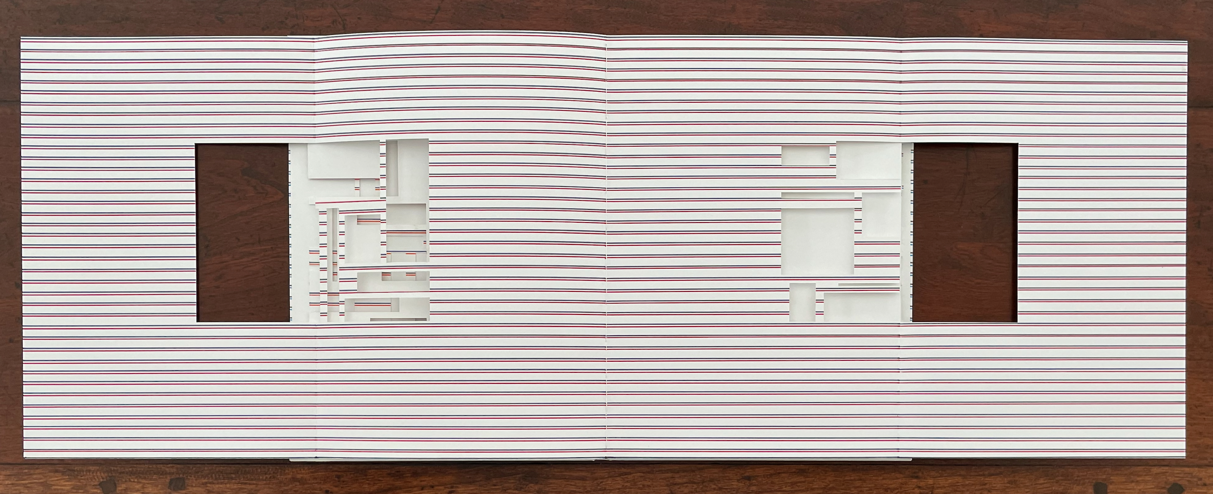 Open book with white pages featuring horizontal red and blue stripes, displaying cut-out shapes on the left side.