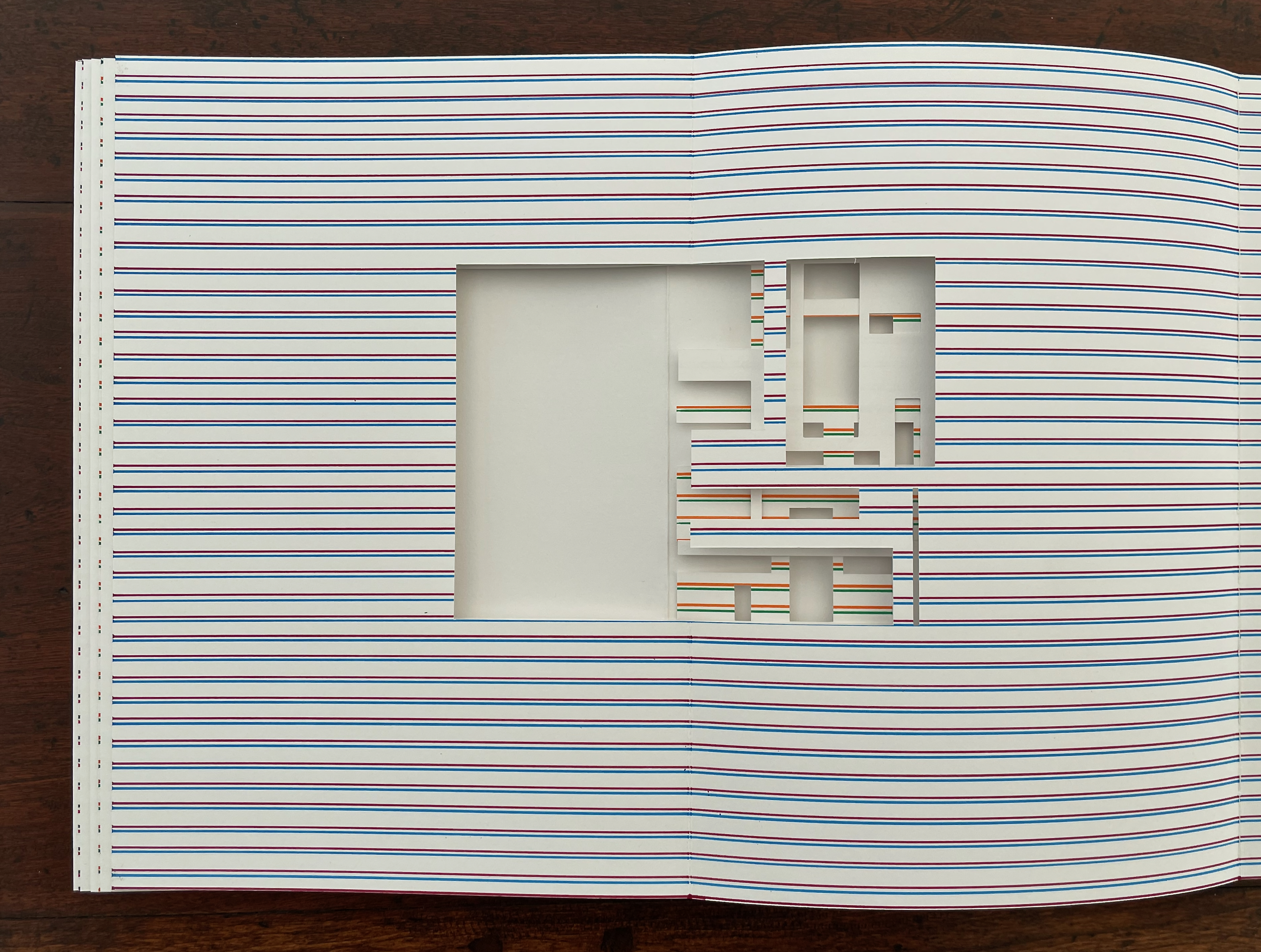 An open book with pages featuring colorful horizontal stripes, revealing a cut-out design in the center.