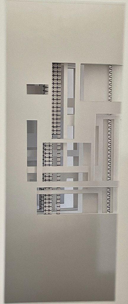 A close-up view of a white architectural model featuring intricate cut-out patterns and varying geometric shapes.