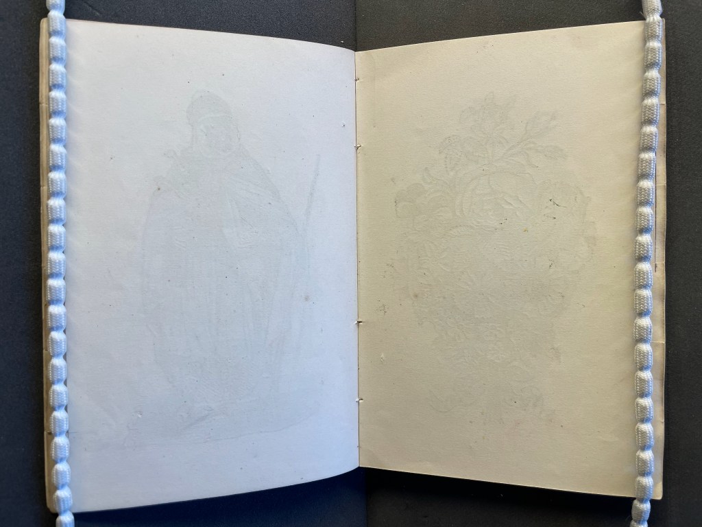 An open book displaying faint illustrations on the pages, one depicting a cloaked figure and the other a floral design, set against a dark background.