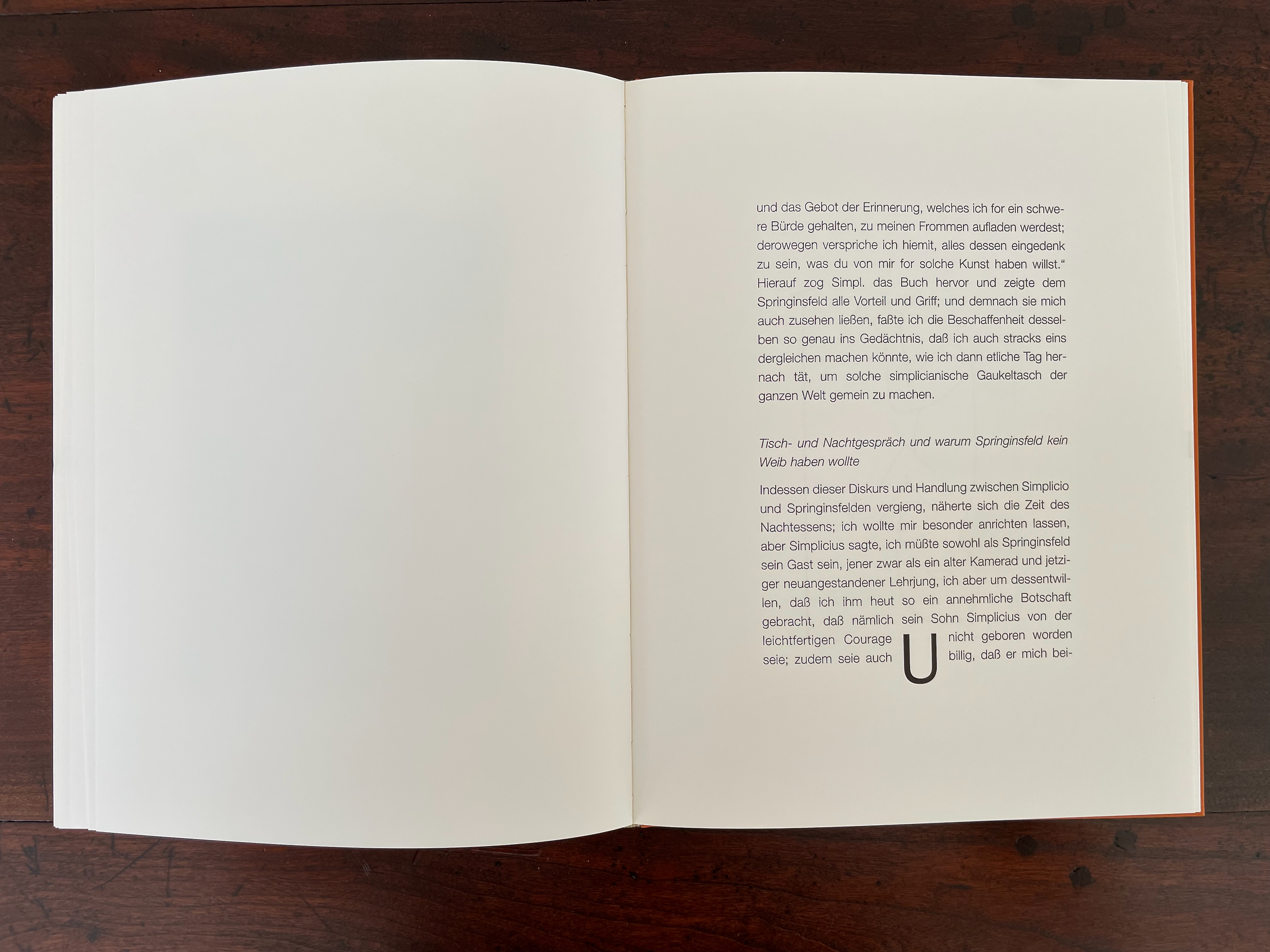 An open book page displaying a large block of German text with some design elements, set against a wooden surface.