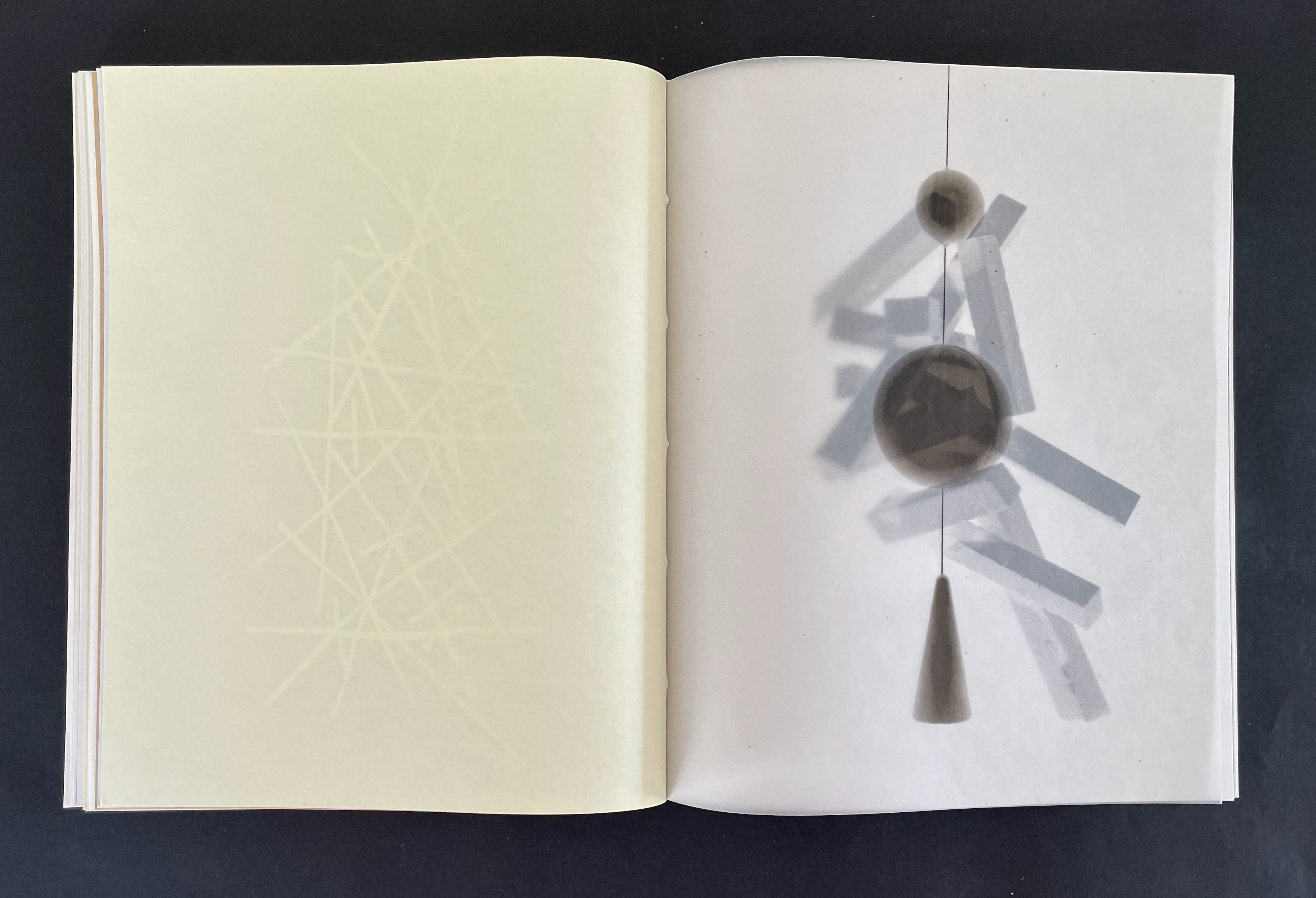 An open book displaying abstract illustrations on its pages, featuring a light yellow background on the left and a darker, shadowy composition of shapes and forms on the right.