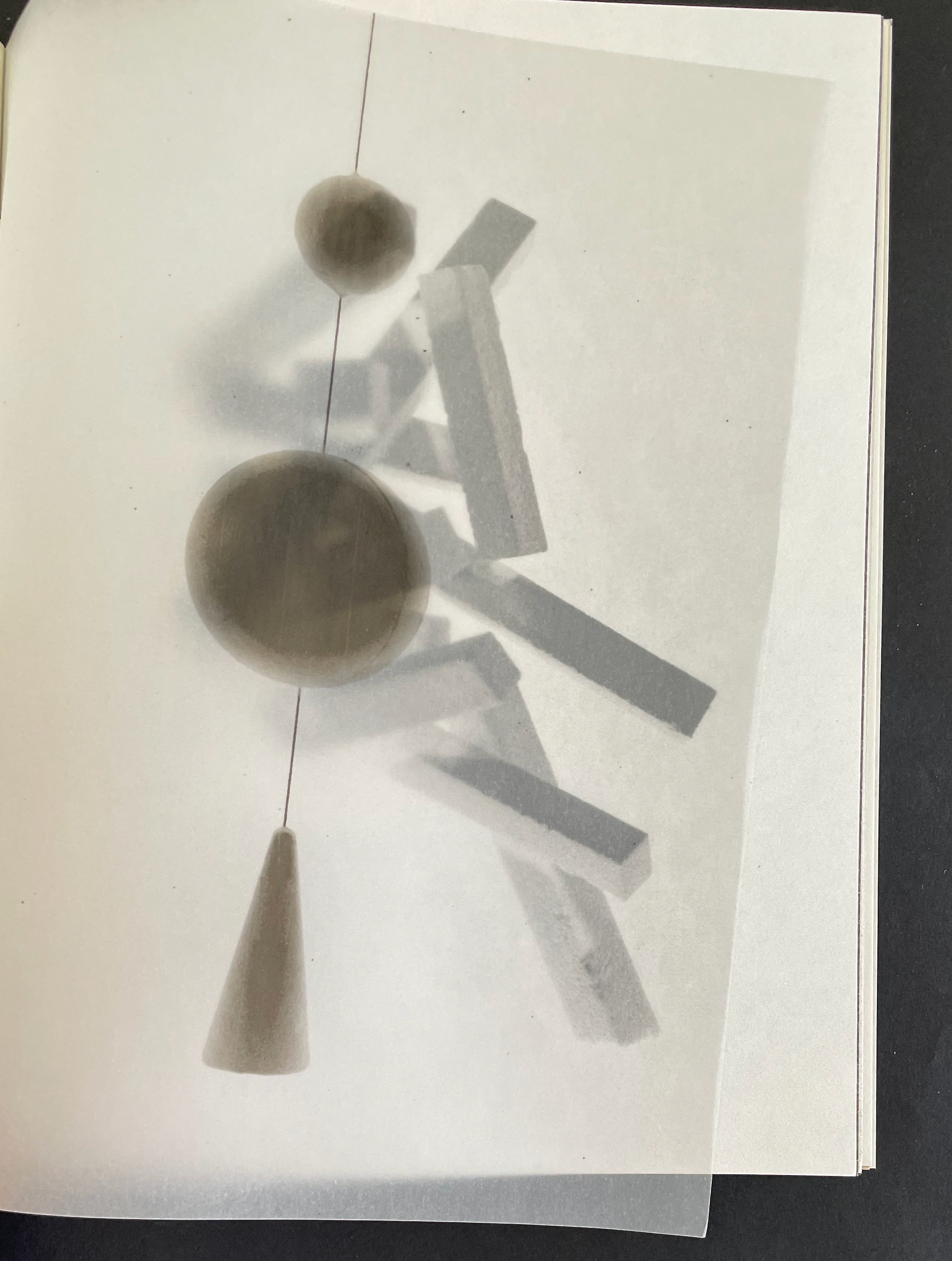 Abstract composition featuring geometric shapes, including spheres and cones, casting shadows on layered paper.